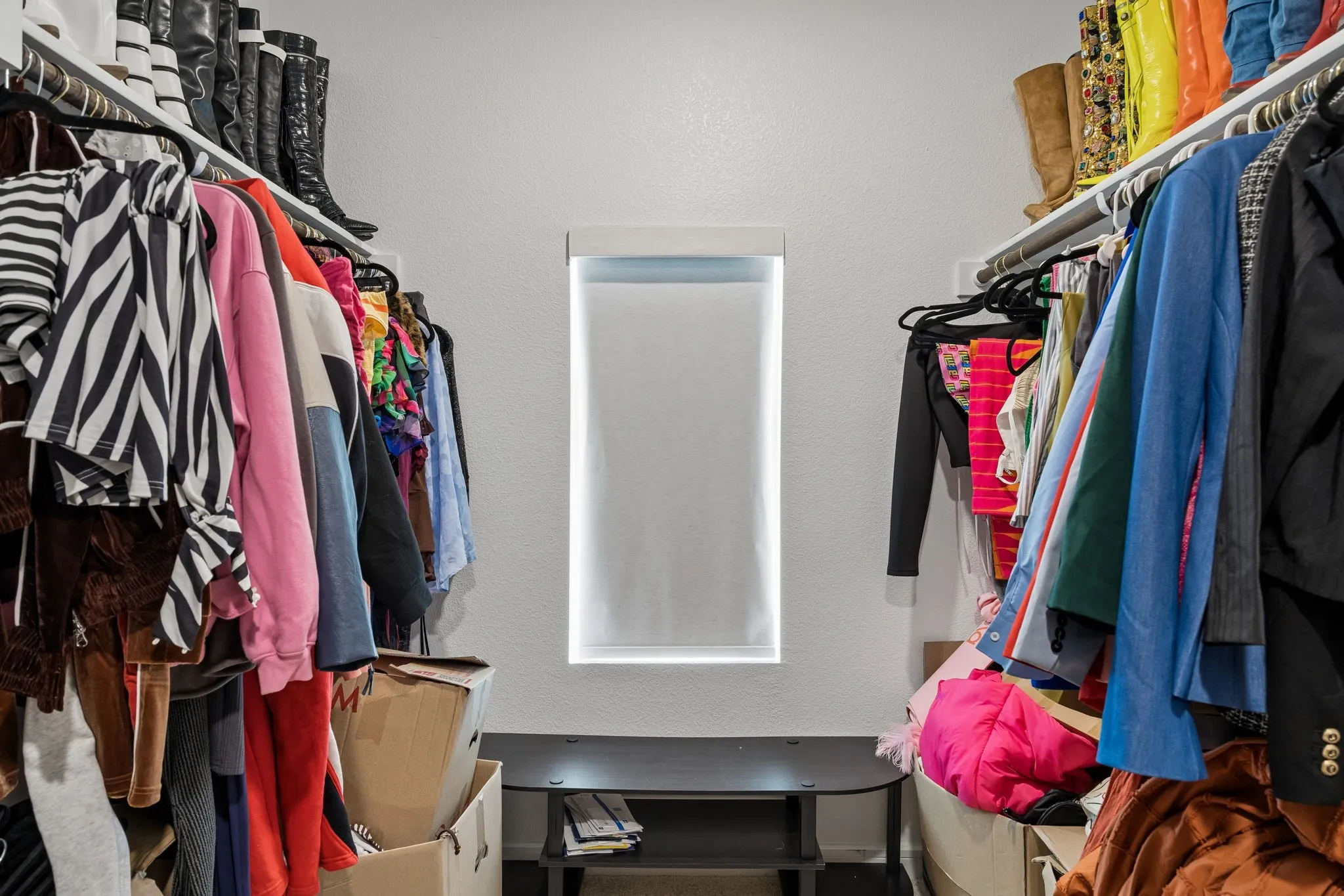 Walk-in closet featuring extensive built-in shelving, hanging rods, and a central window with roller shade