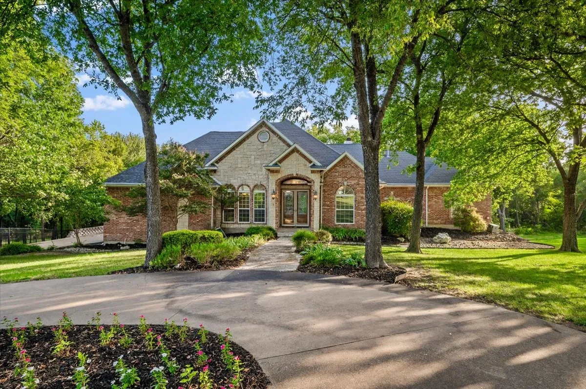 Brick and stone facade residence featuring a dark shingle roof and a paved driveway