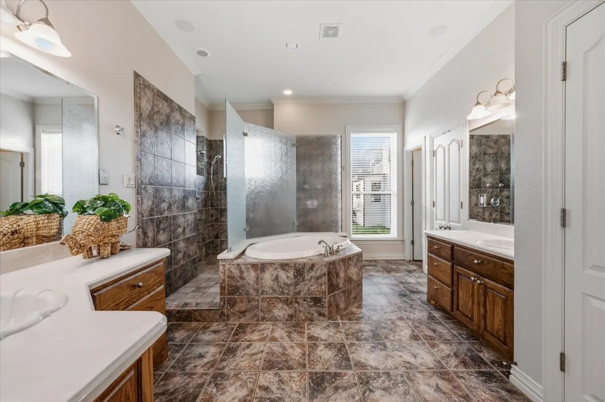 Spacious bathroom featuring a built-in soaking tub, a separate glass-enclosed shower, dual vanity sinks with light countertops, and wood-finish cabinetry