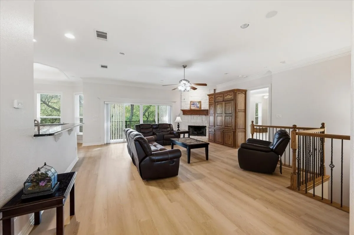 Open-concept living area featuring light wood-finish flooring, a white brick fireplace with a wood mantel, a ceiling fan, and recessed lighting