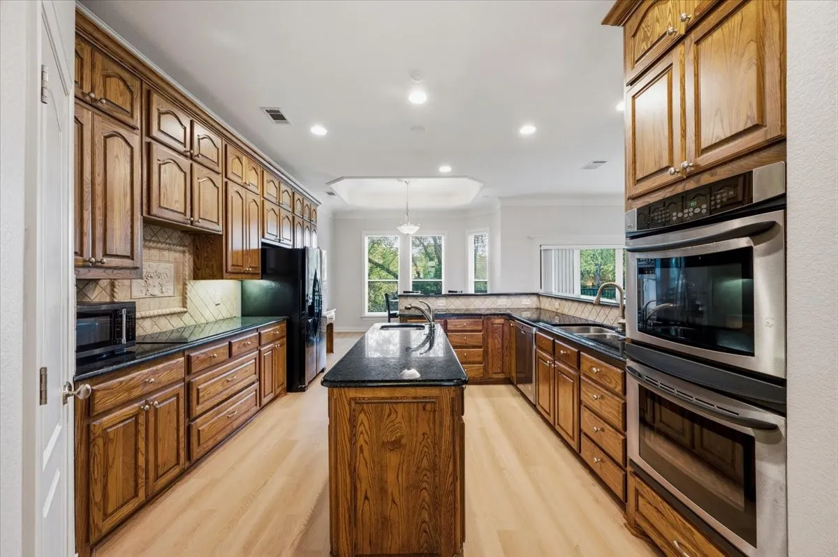 Kitchen featuring wood cabinetry, black countertops, a central island, recessed lighting, and light wood-finish flooring