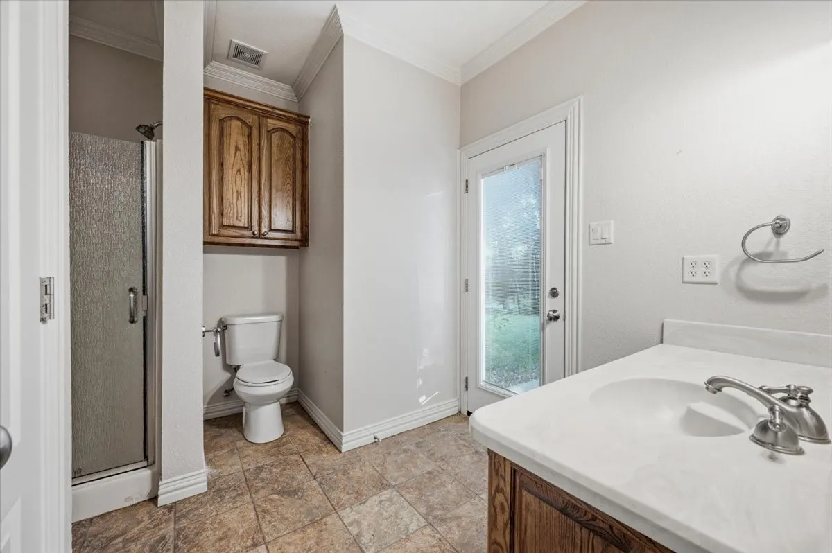 Bathroom featuring a glass-enclosed shower, a vanity with an integrated sink and wood-finish cabinetry, a toilet, and overhead wood-finish wall cabinets