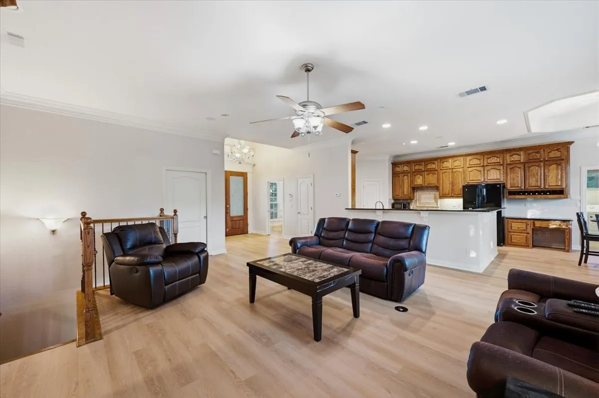 Open-concept living area with wood-finish flooring, a ceiling fan, and crown molding