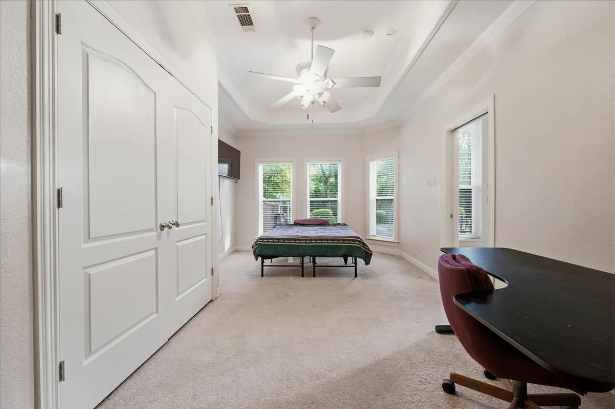 Spacious room featuring light-toned carpet flooring, white trim, and a tray ceiling with a ceiling fan