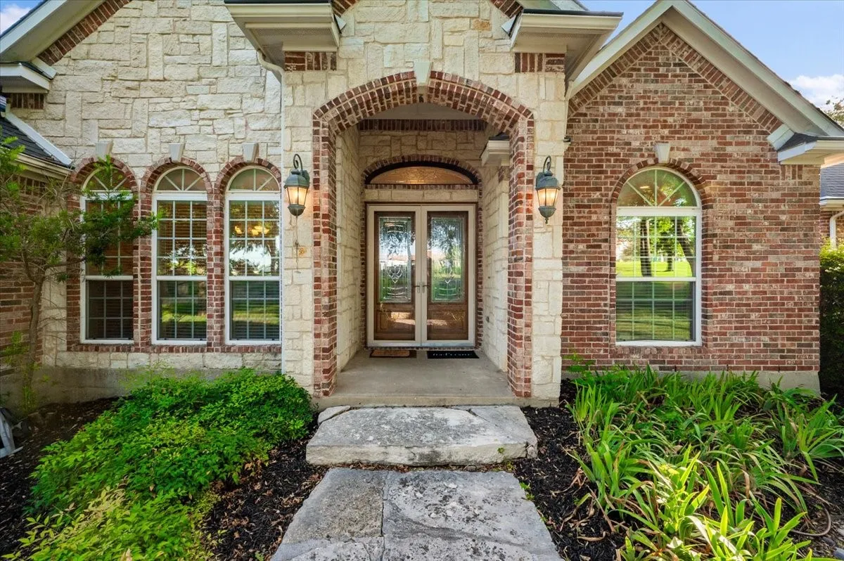 Stone and brick facade featuring an arched entry with double doors and decorative glass