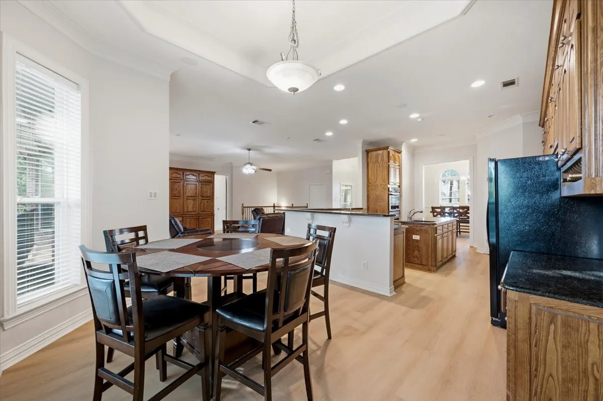 Open-concept living space featuring wood-finish flooring, recessed lighting, a tray ceiling, and a kitchen with dark cabinetry and black appliances