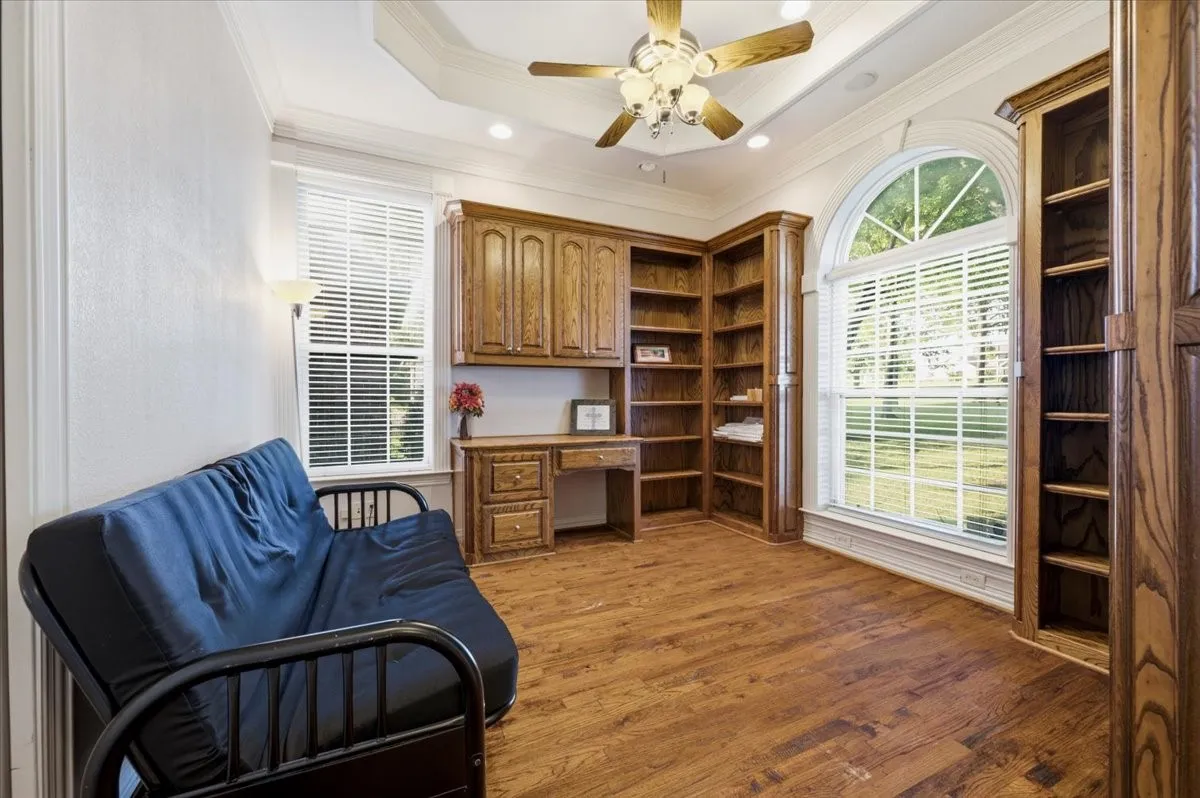 Office featuring, built in wood cabinets and desk, raised ceiling, ceiling fan, overlooking the gorgeous yard.