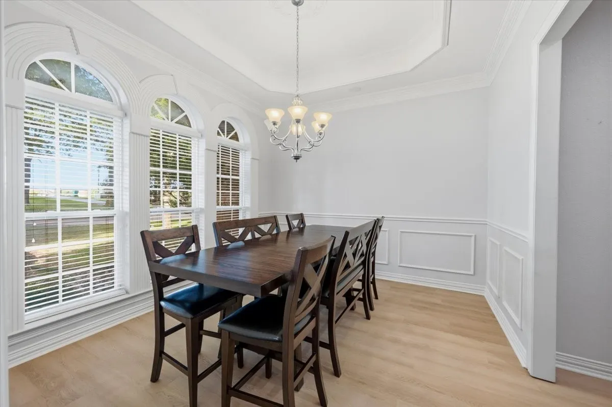 Room featuring multiple arched windows, crown molding, wainscoting, a tray ceiling, and light wood-finish flooring