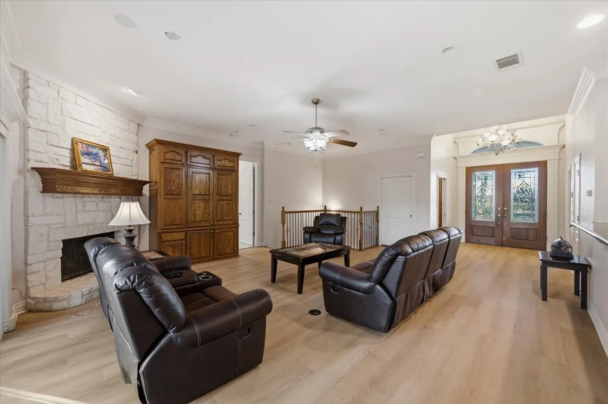 Spacious living area featuring a stone fireplace with a wood mantel, light wood-finish flooring, and a decorative double-door entry