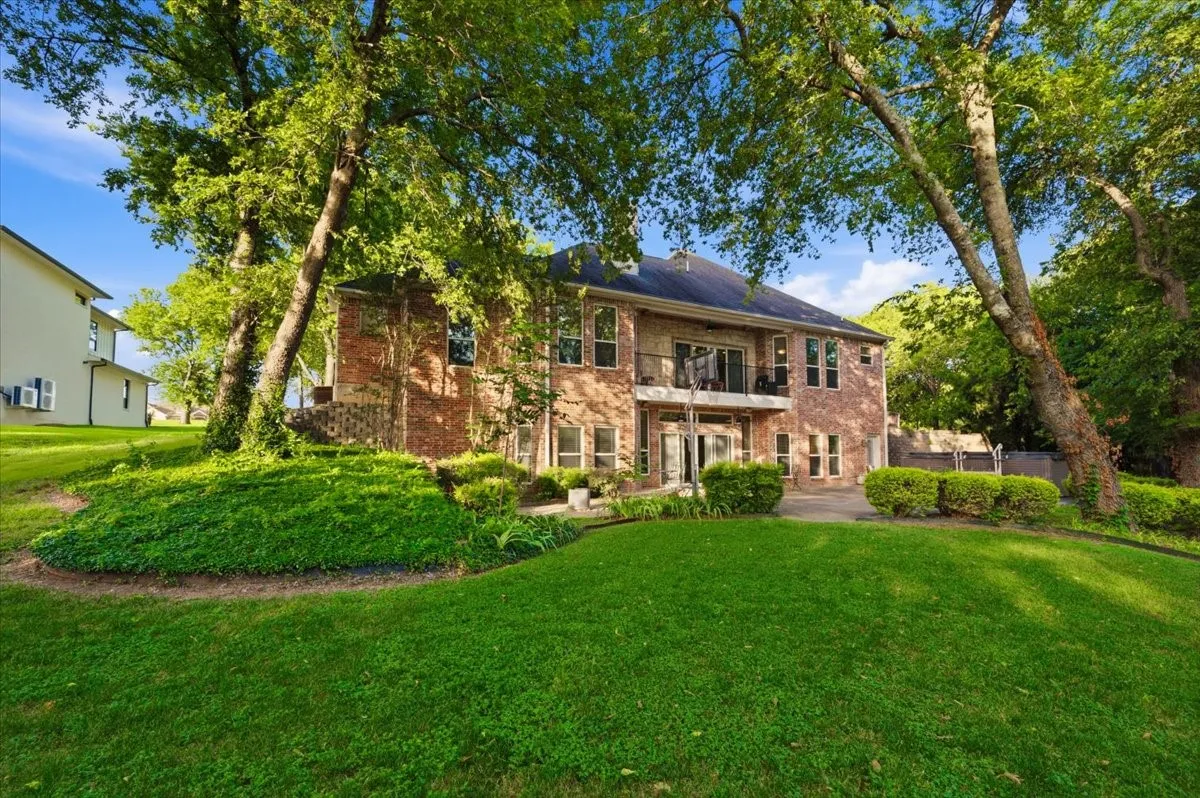 Expansive rear facade featuring brick construction, a second-story balcony with metal railing, multiple windows, and a lower-level patio