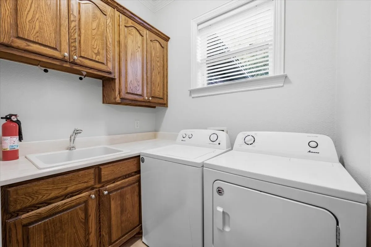 Utility room featuring wood cabinetry, a white countertop, an integrated utility sink with a chrome faucet, and a window with blinds