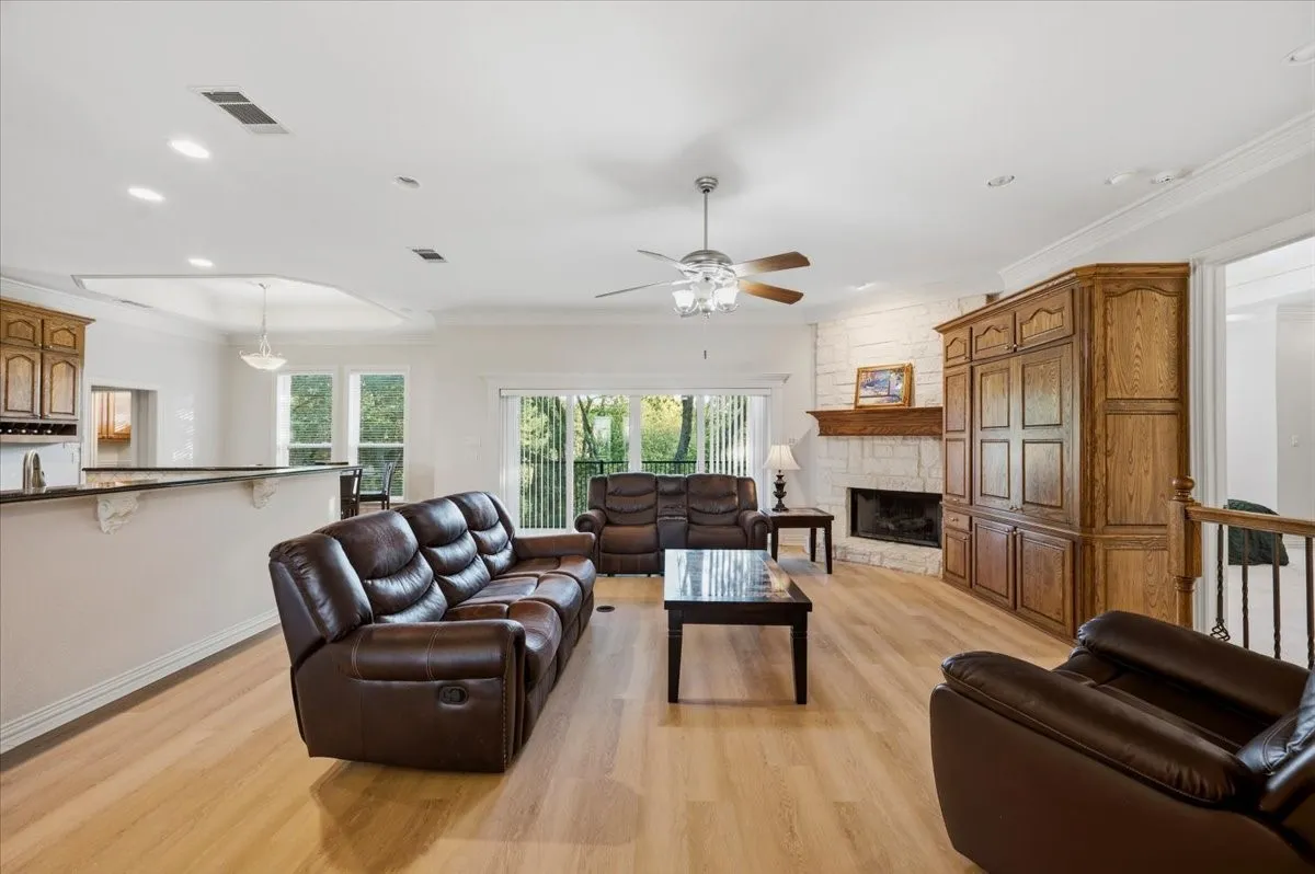 Spacious living area featuring light wood-finish flooring, a stone-faced fireplace with a wood mantle, a built-in entertainment center, recessed lighting, and a ceiling fan