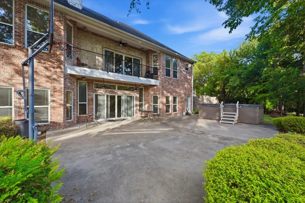 Expansive concrete patio with dual hot tubs and surrounding mature greenery