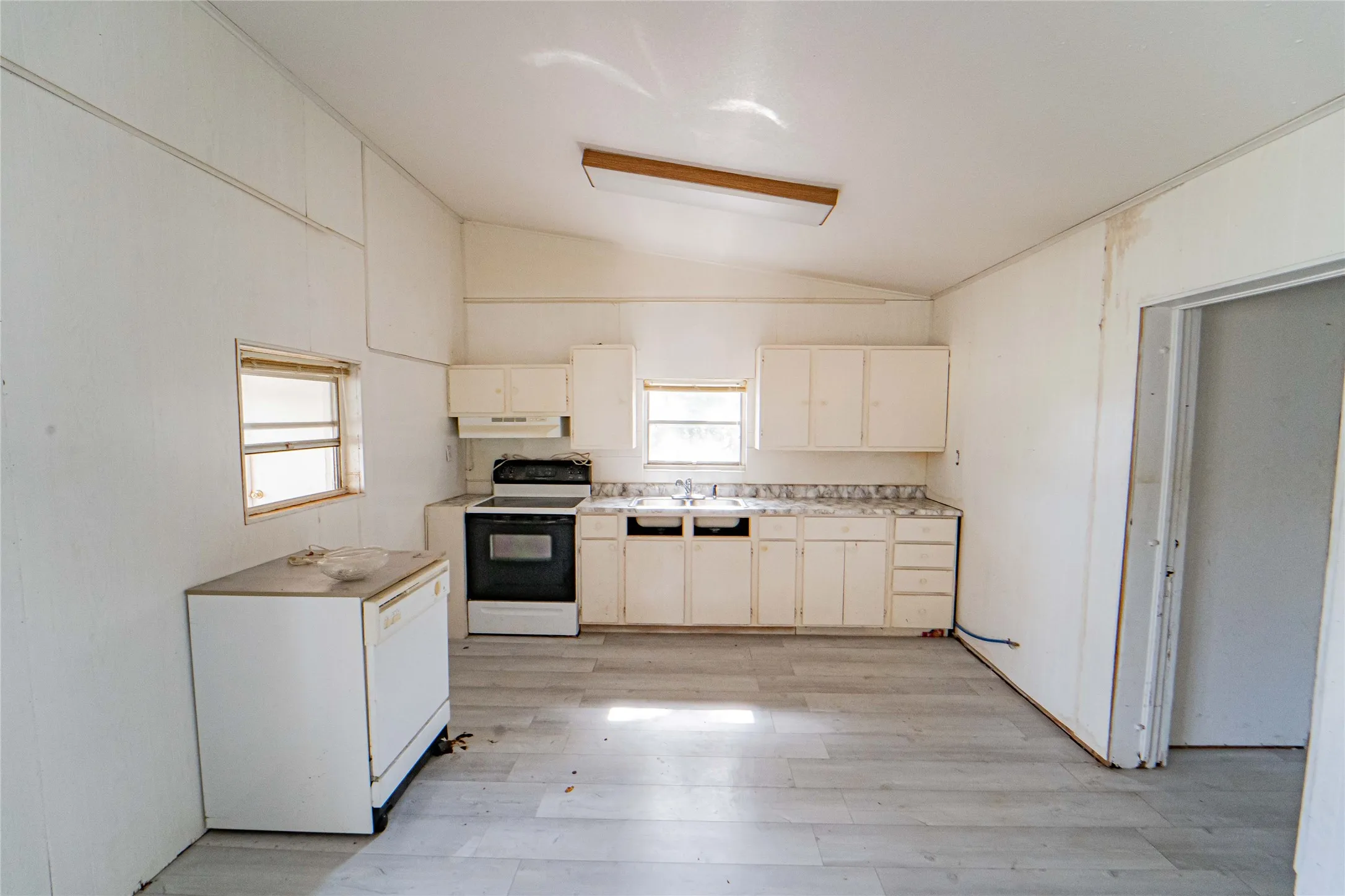 Kitchen  in Guest Quarters, featuring light wood-finish flooring, white cabinetry, a built-in range, and a dual-basin sink with a window above