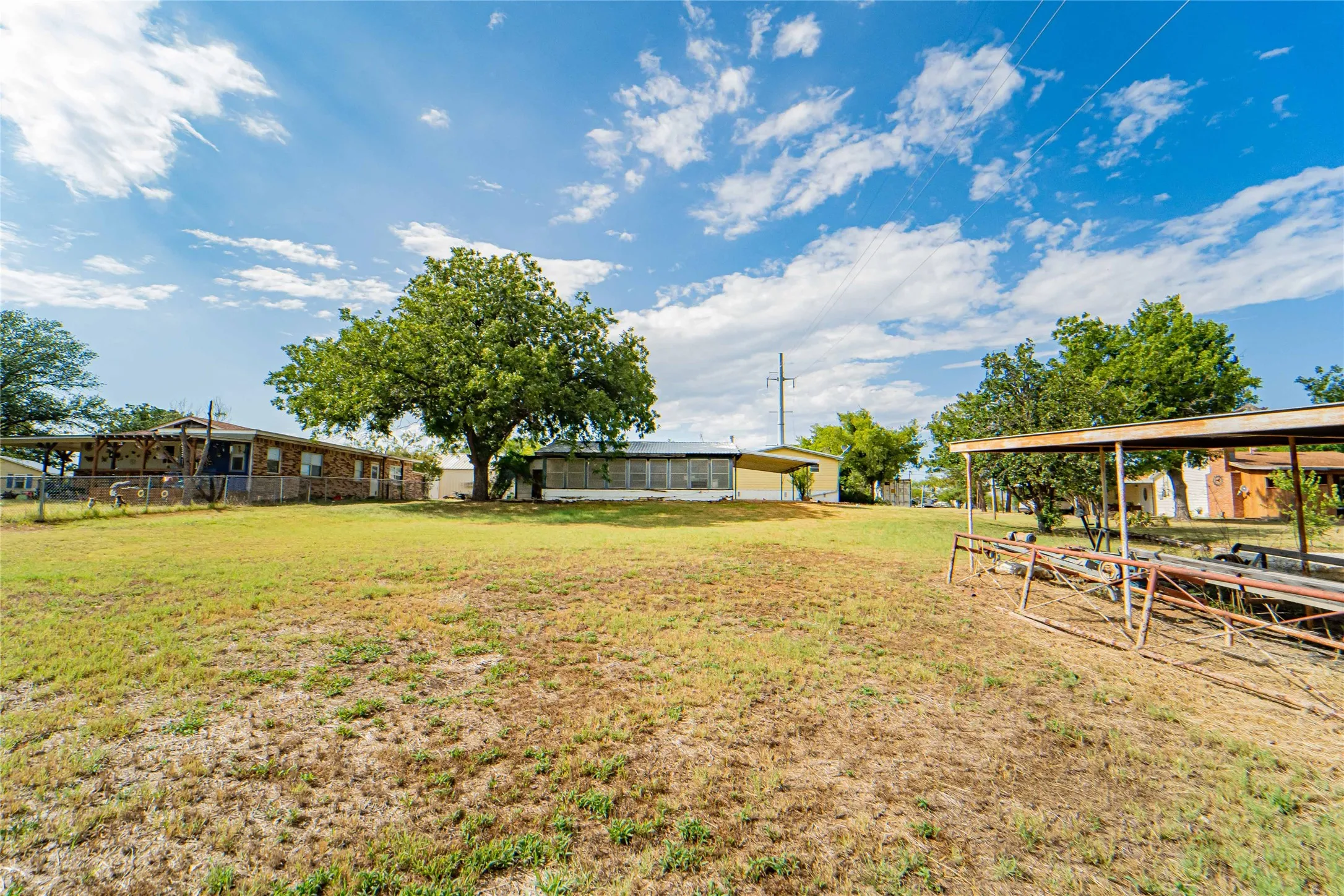 Expansive open lot with a substantial mature tree and a covered metal structure