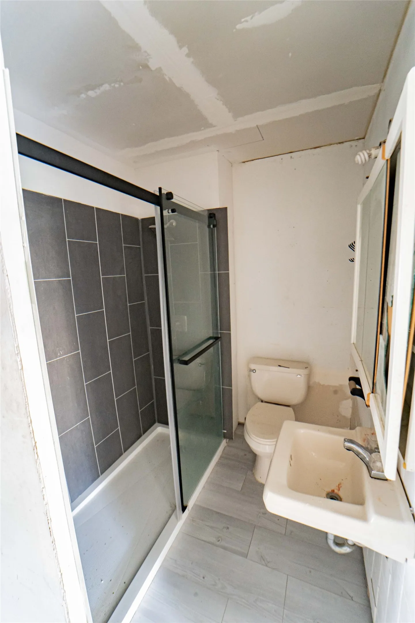 Guest Quarters Bathroom featuring a tub with sliding glass doors, dark gray subway tile surround, and a coordinating light gray tile floor