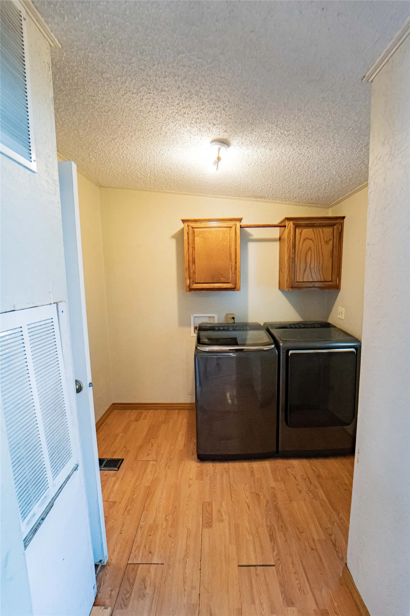 Laundry area, conveniently located to kitchen and bedrooms,  featuring wood-finish flooring, overhead lighting, and two wall-mounted wood-finish cabinets