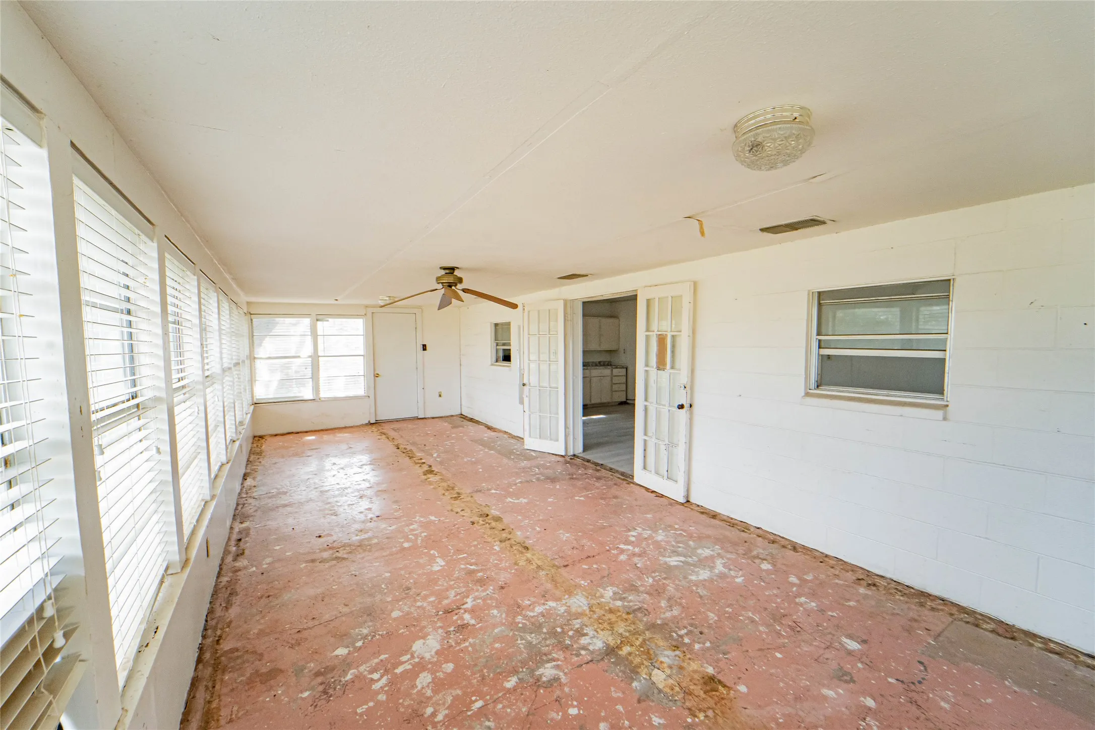 Enclosed sunroom featuring multiple large windows with blinds, a ceiling fan, and double French doors