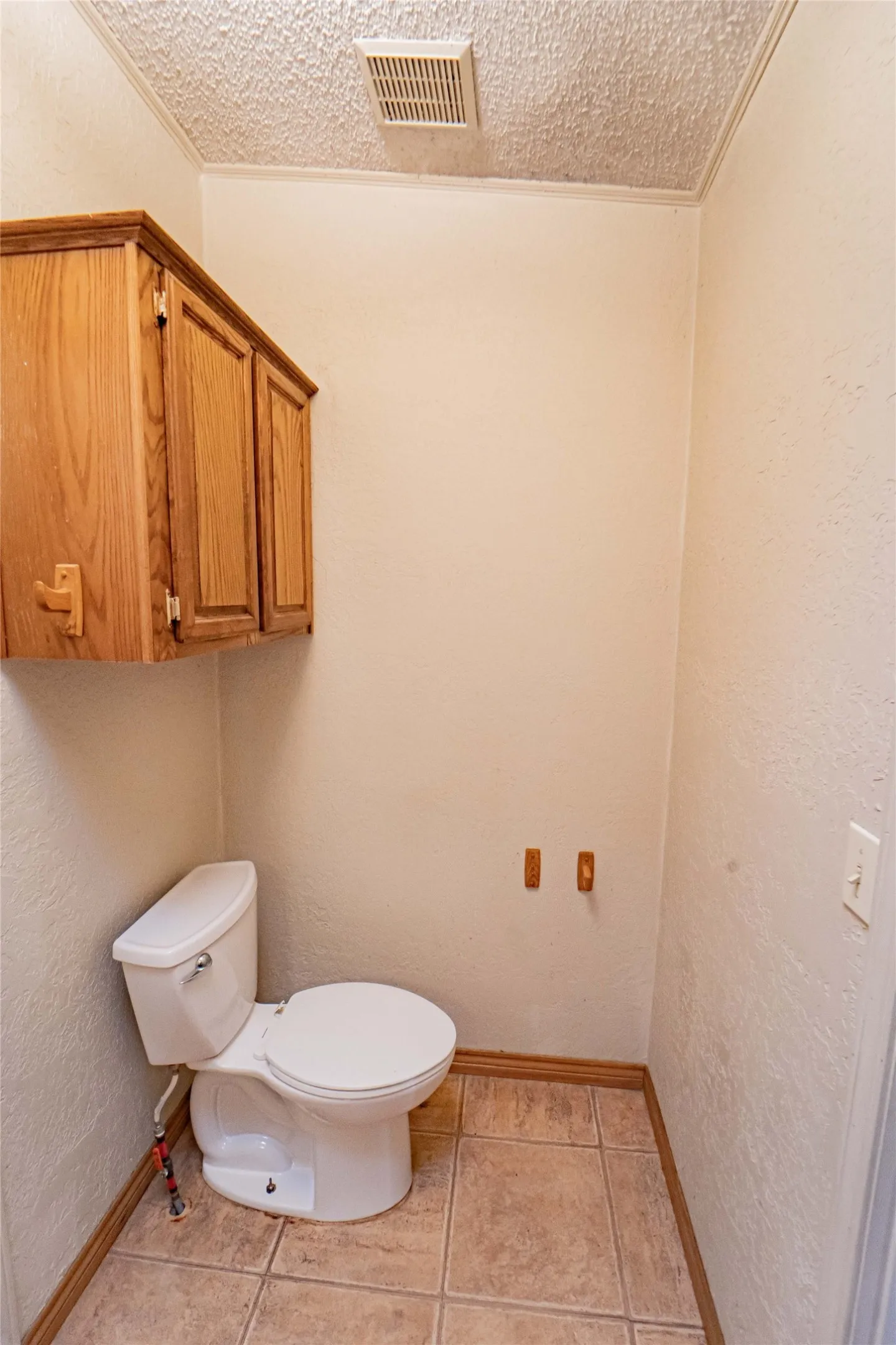 Restroom featuring a white toilet, wood-finish wall cabinetry, tiled flooring, wood baseboards, and a ceiling-mounted ventilation fan