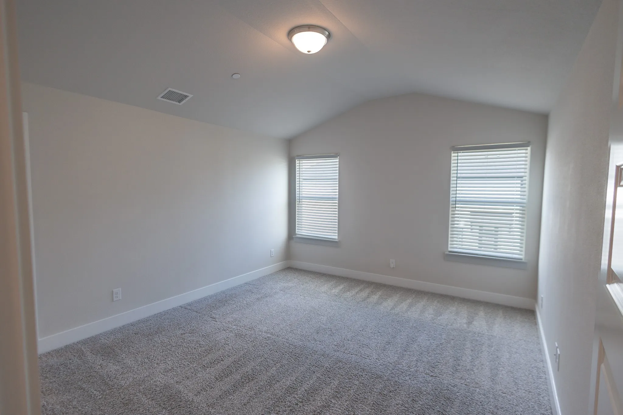 Neutral wall color, vaulted ceiling, two casement windows, white window trim, and plush carpet flooring