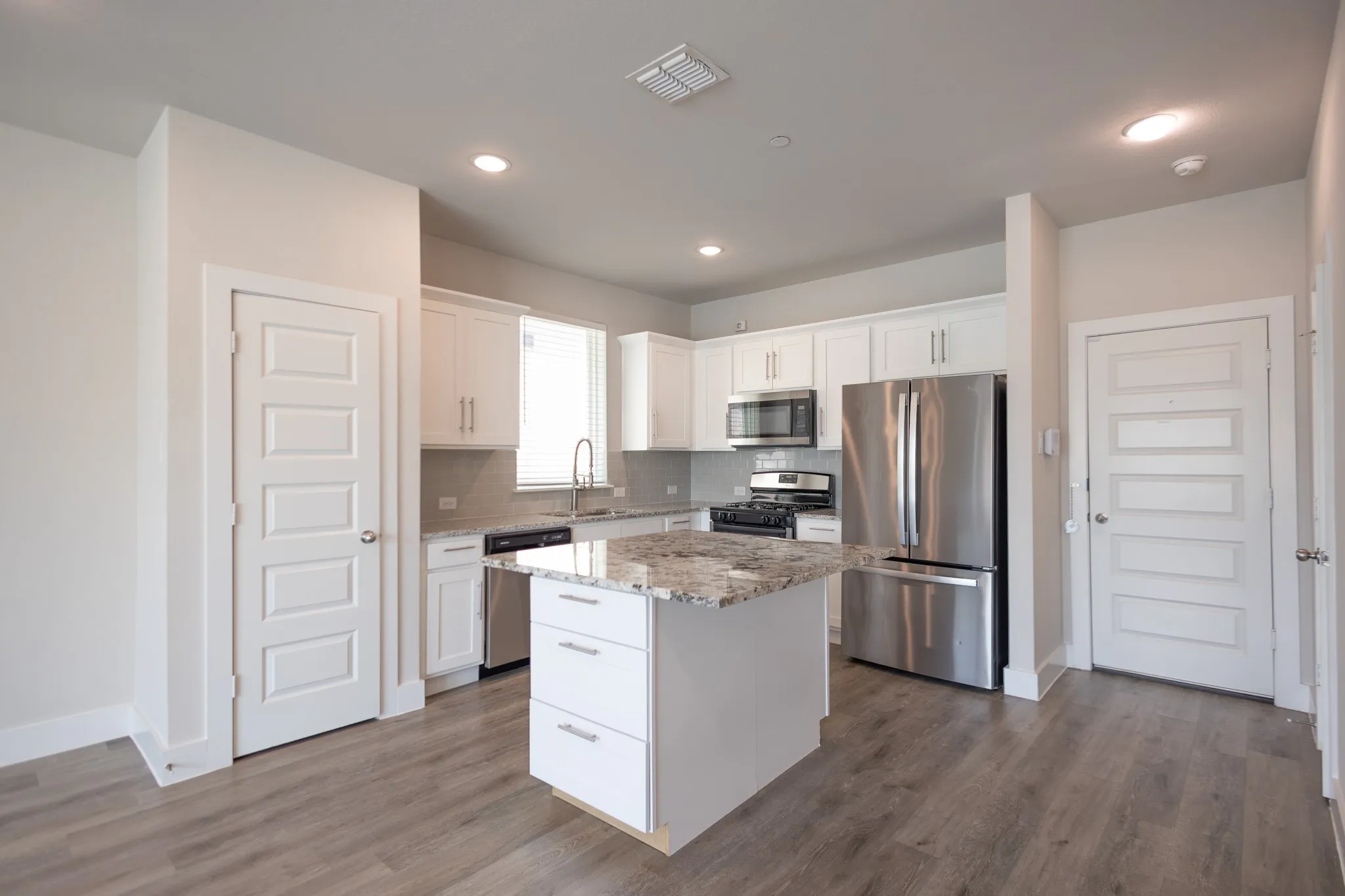 Open-concept living space featuring a kitchen island with stone countertop, stainless steel appliances, wood-finish flooring, and recessed lighting