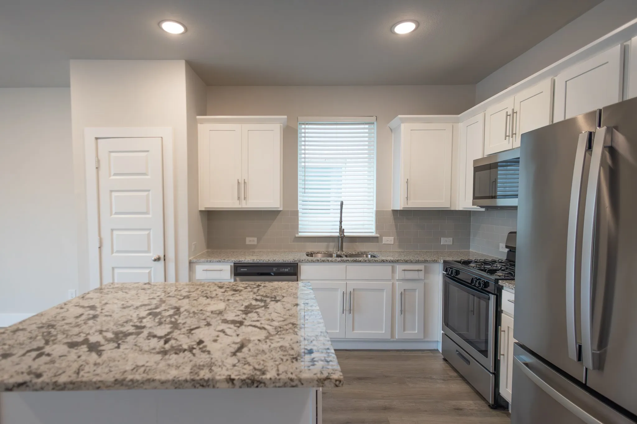 Open-concept living space featuring wood-finish flooring, recessed lighting, and a modern kitchen island with a stone countertop