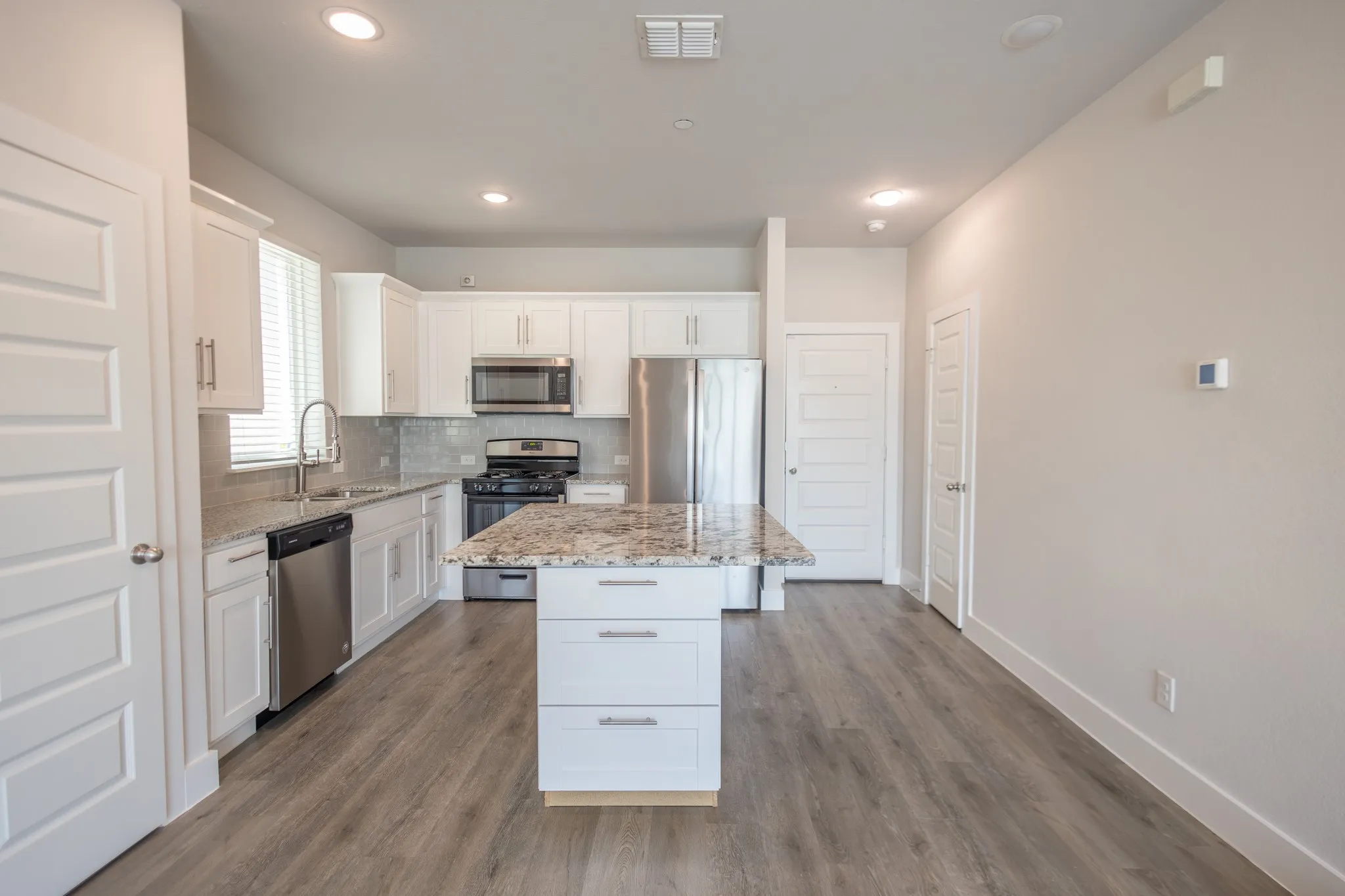 Kitchen featuring an island with stone countertop, stainless steel appliances, white cabinetry, wood-finish flooring, and recessed lighting