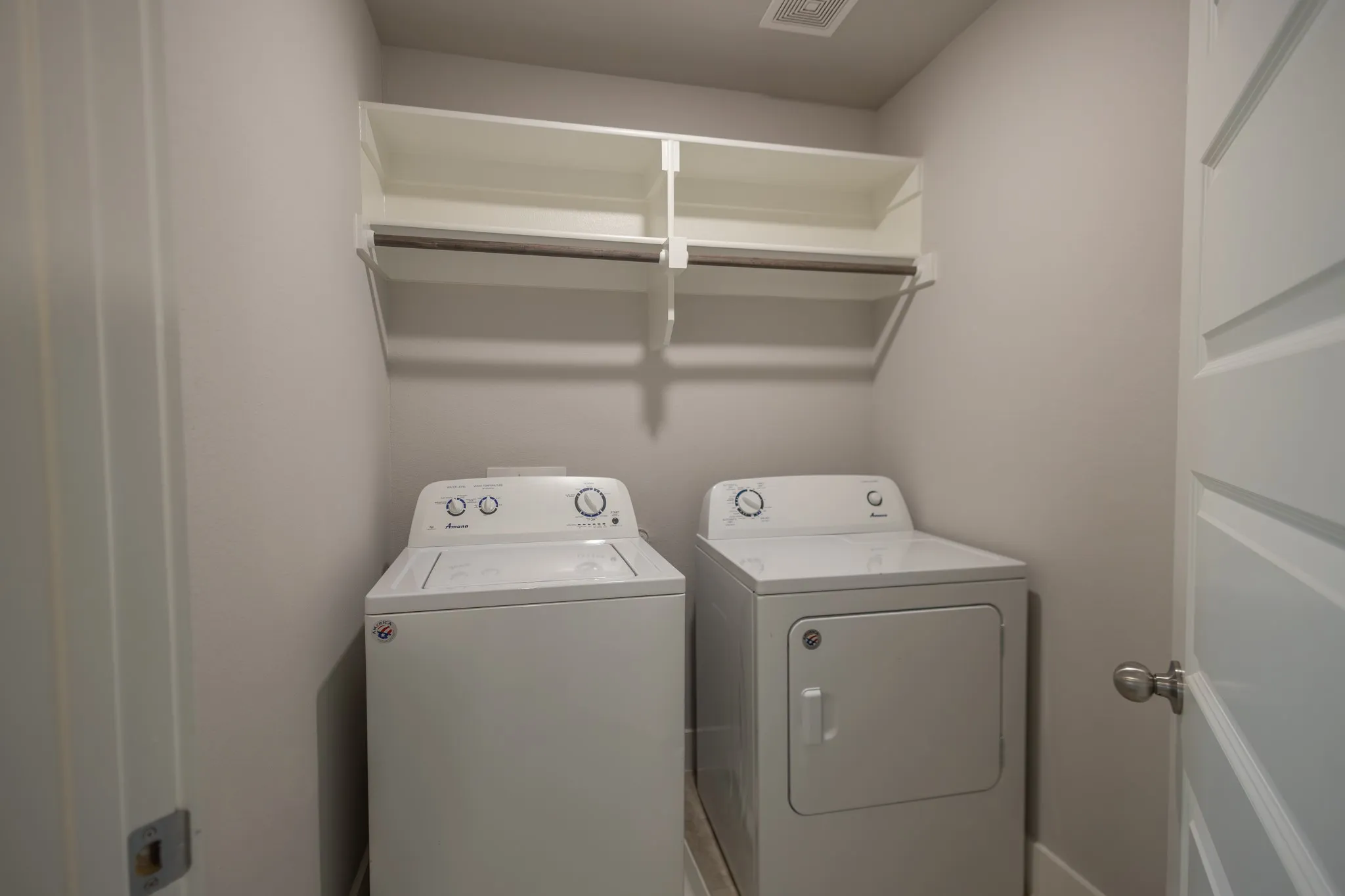 Dedicated laundry area featuring built-in white shelving, wood-finish hanging rod, and tile flooring
