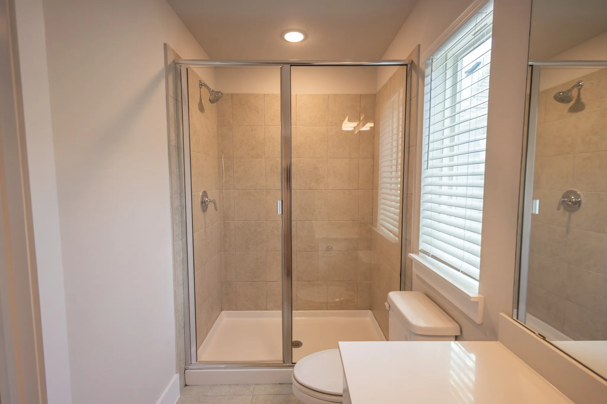 Full bathroom featuring a white vanity with an integrated sink and light countertop, chrome faucet, and a large frameless mirror

