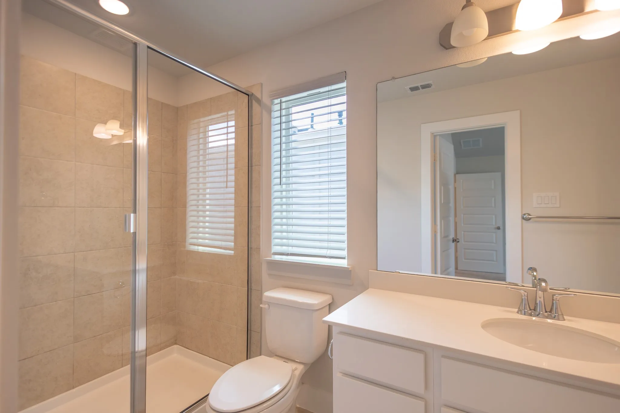 Glass-enclosed shower with a built-in shelf, neutral-toned tile surround, and a white shower pan