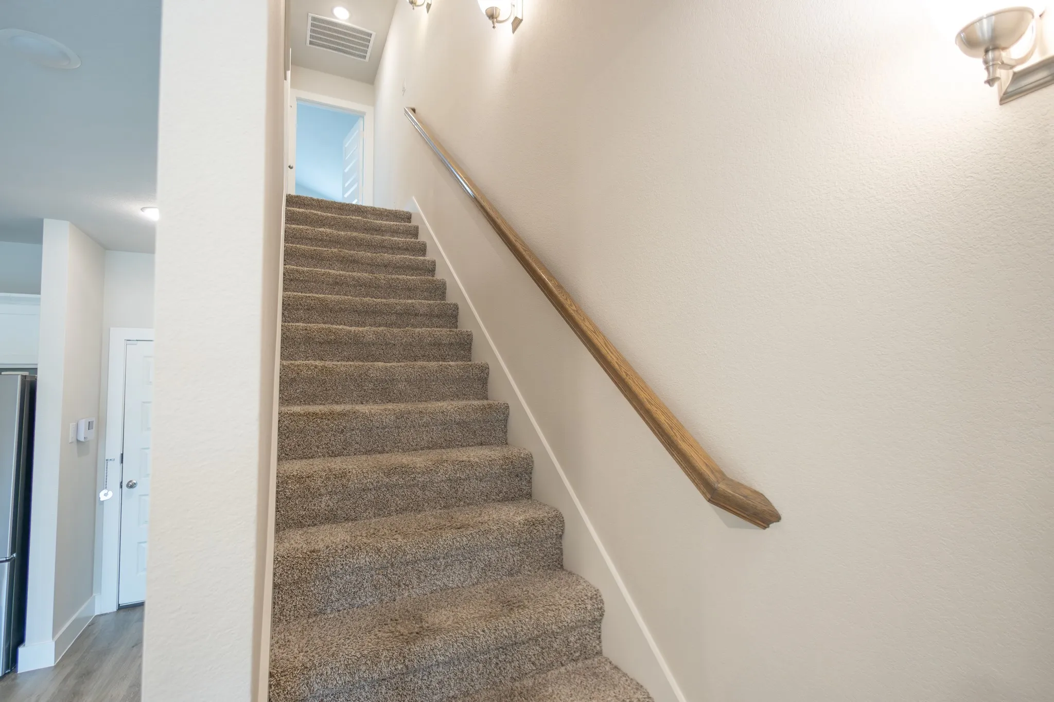 Carpeted staircase featuring a light wood-finish handrail