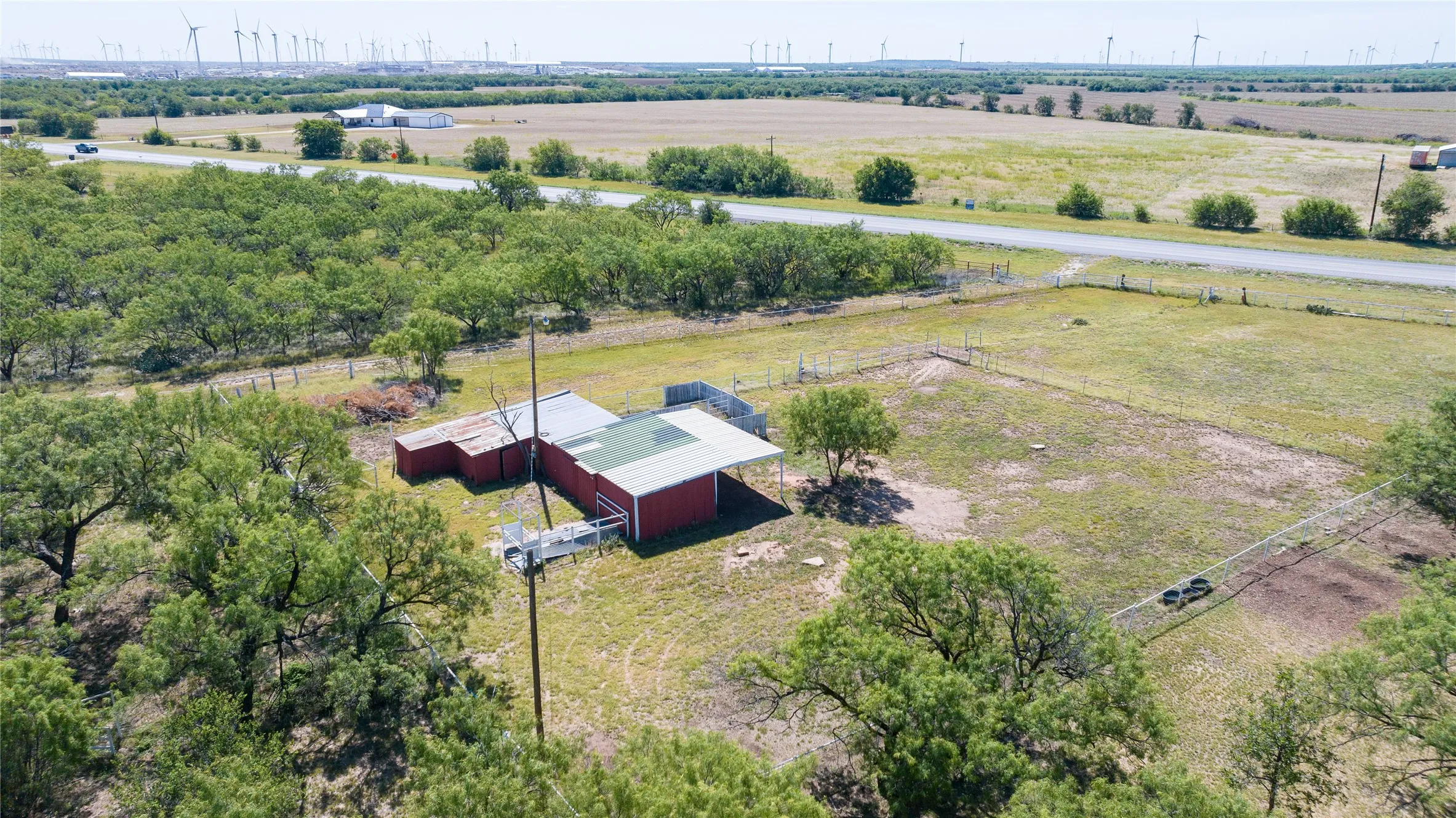 Red barn structure with a metal roof, situated on a grassy lot surrounded by mature trees