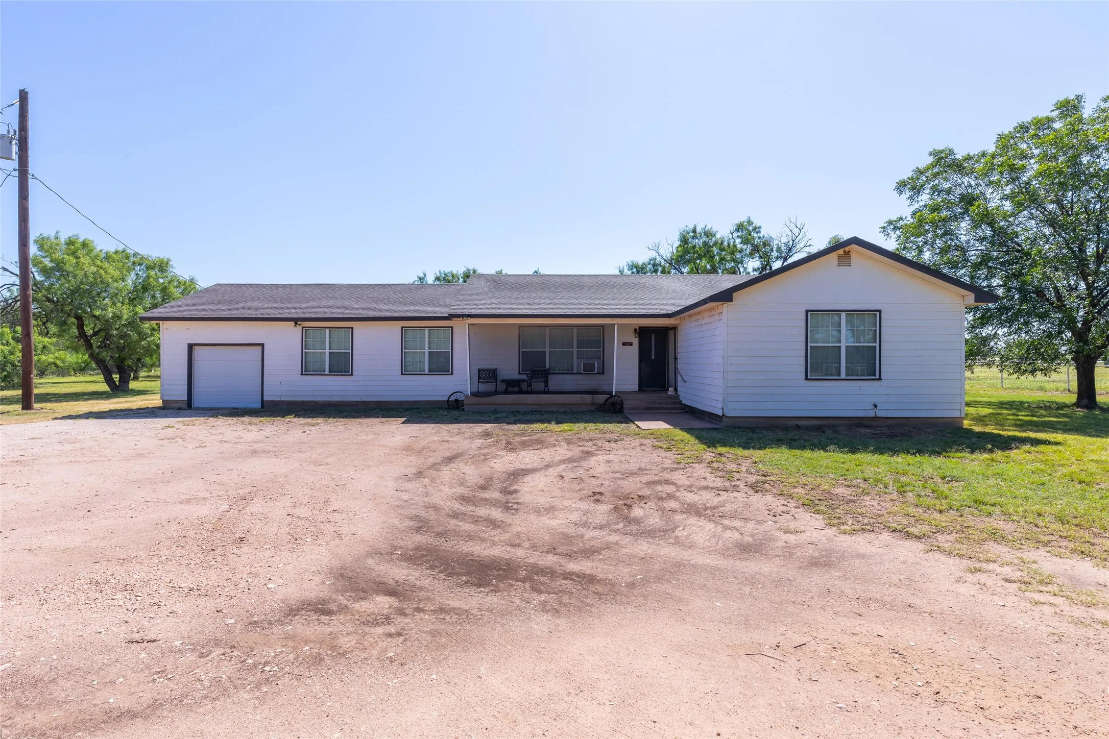 Ranch-style exterior featuring white siding, a dark shingle roof, and a covered porch