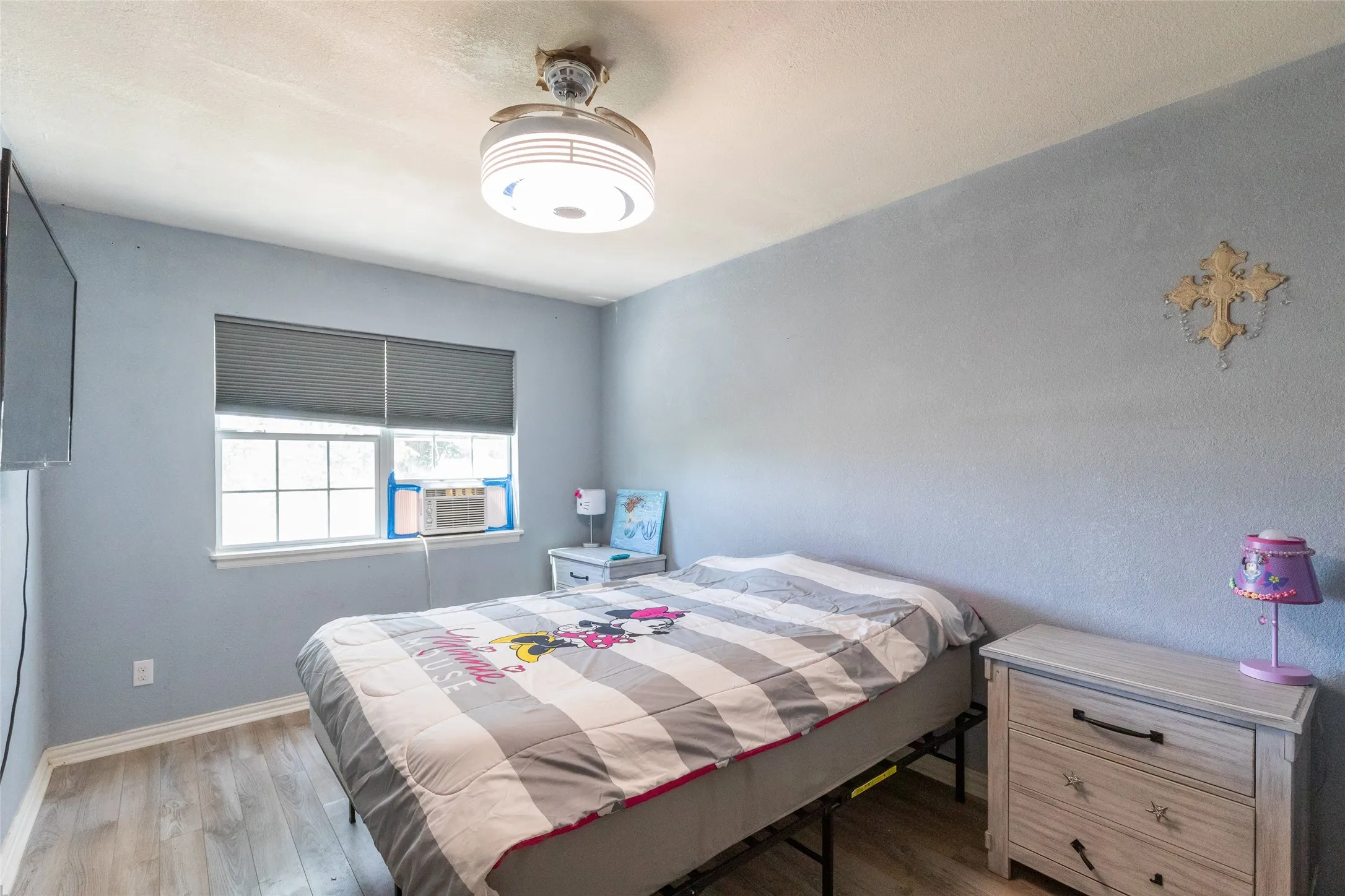 Bedroom featuring light blue walls, wood-finish flooring, and a ceiling fan with integrated lighting