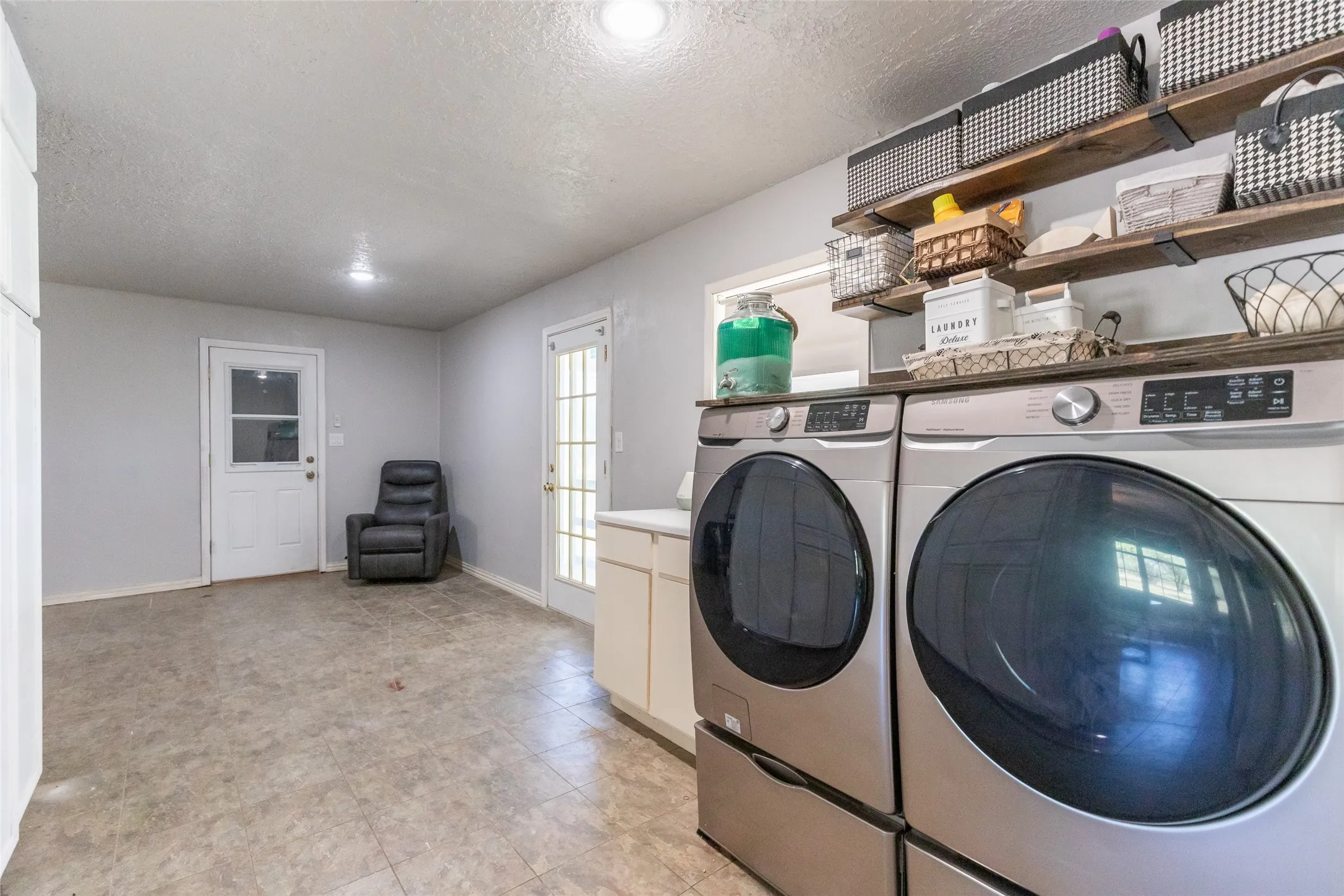 Utility room with light gray walls, built-in cabinetry, and wood-finish open shelving