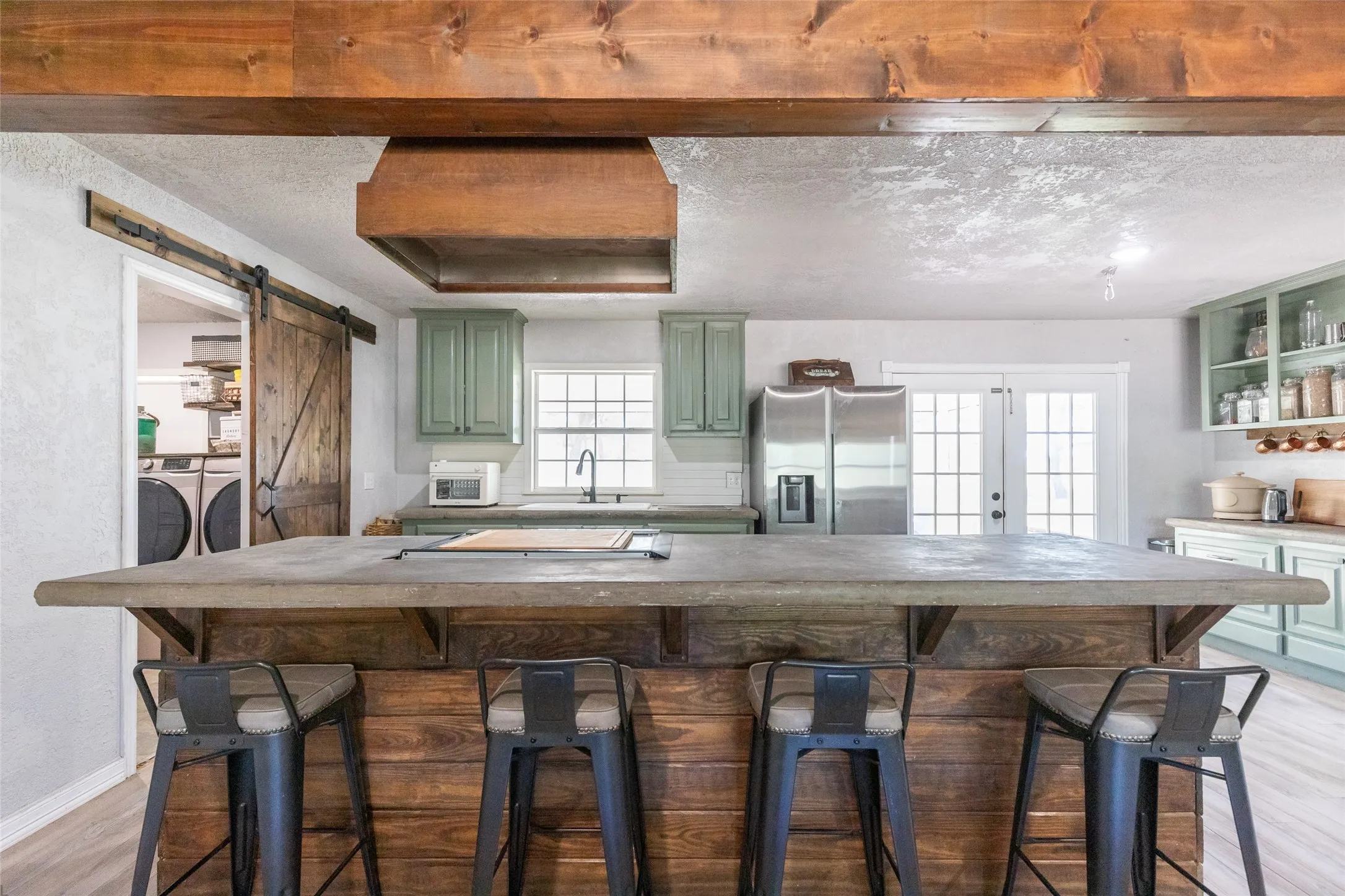 Kitchen featuring a wood-clad island with seating, sage-green cabinetry, stainless steel appliances, and French doors