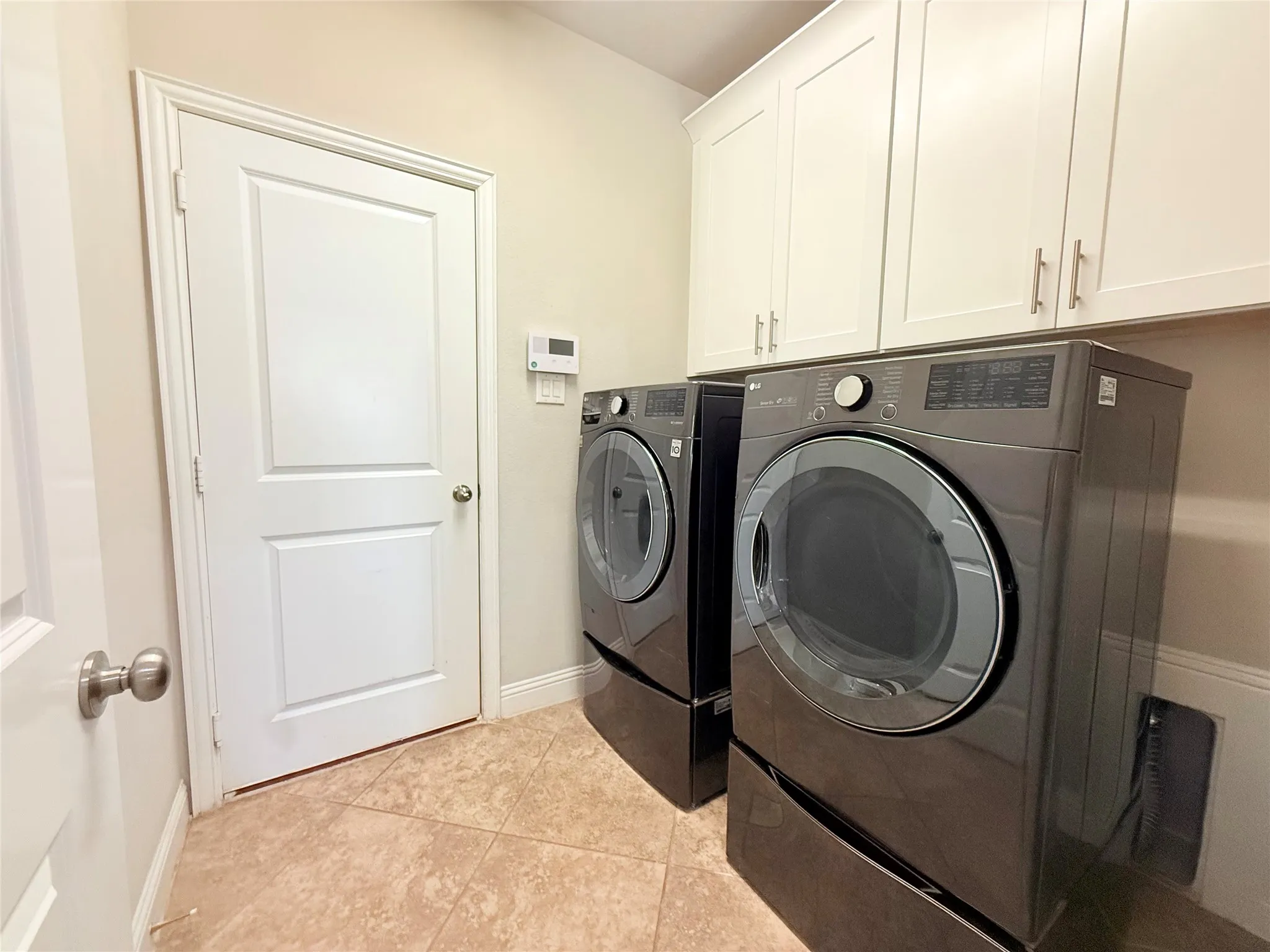 Laundry area featuring white shaker-style cabinetry with brushed nickel hardware, neutral-toned wall paint, and tiled flooring