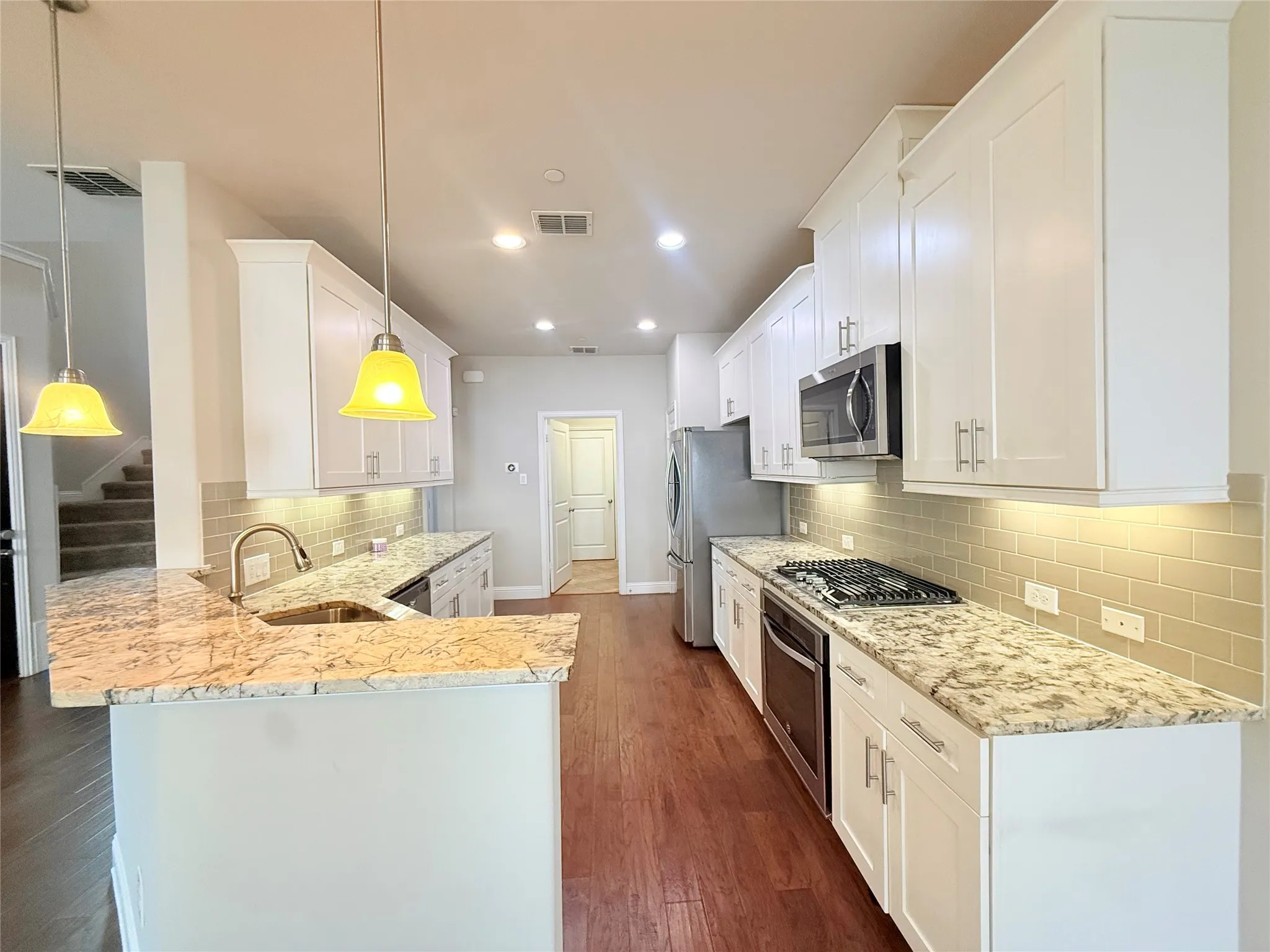 Kitchen featuring white cabinetry, light-toned granite countertops, stainless steel appliances, and wood-finish flooring