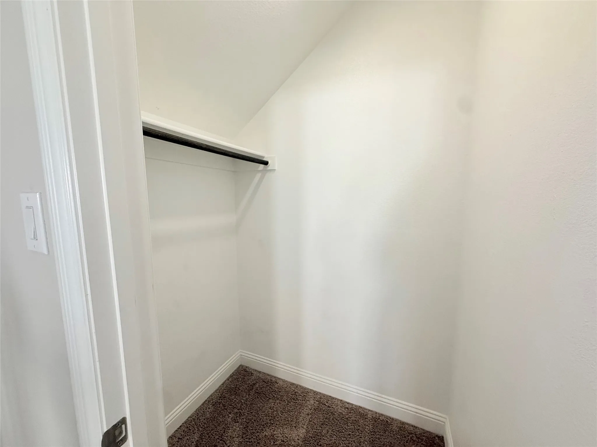 Compact closet featuring a built-in shelf and clothing rod, textured walls, baseboards, and carpet flooring