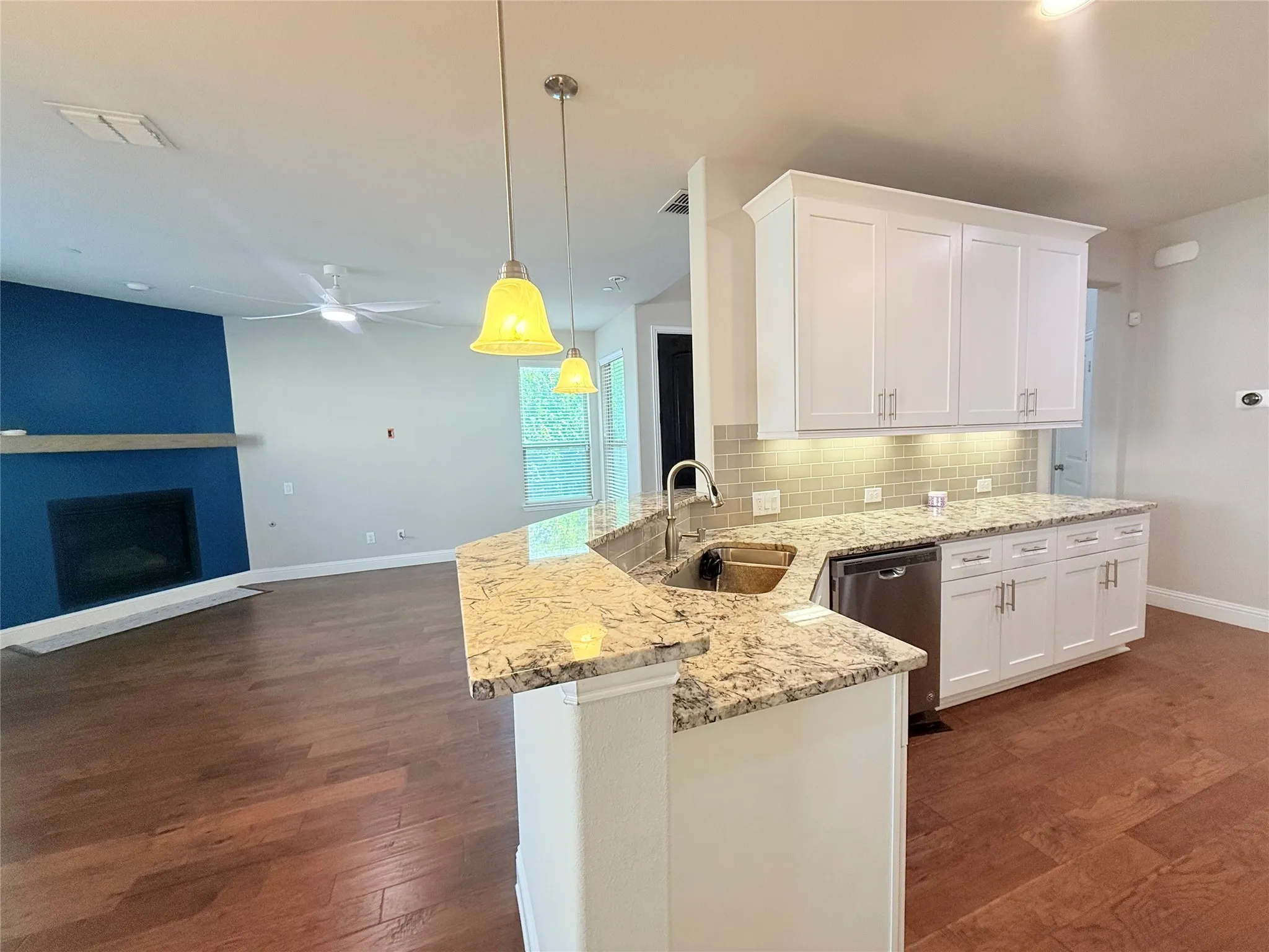 Kitchen island with granite countertops, undermount sink, stainless steel dishwasher, and overhead pendant lighting