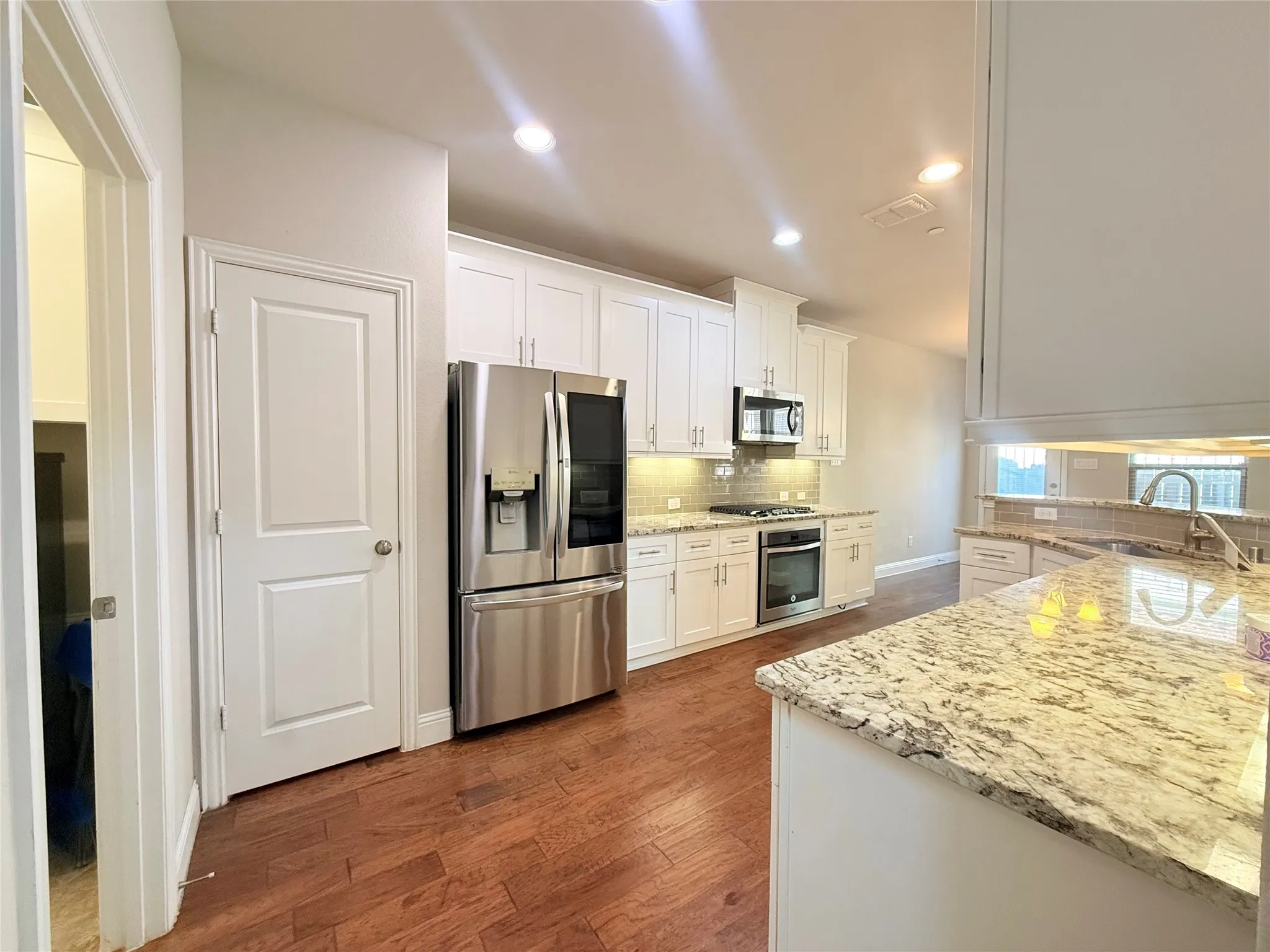 Modern kitchen featuring light-toned granite countertops, white cabinetry, stainless steel appliances, and wood-finish flooring