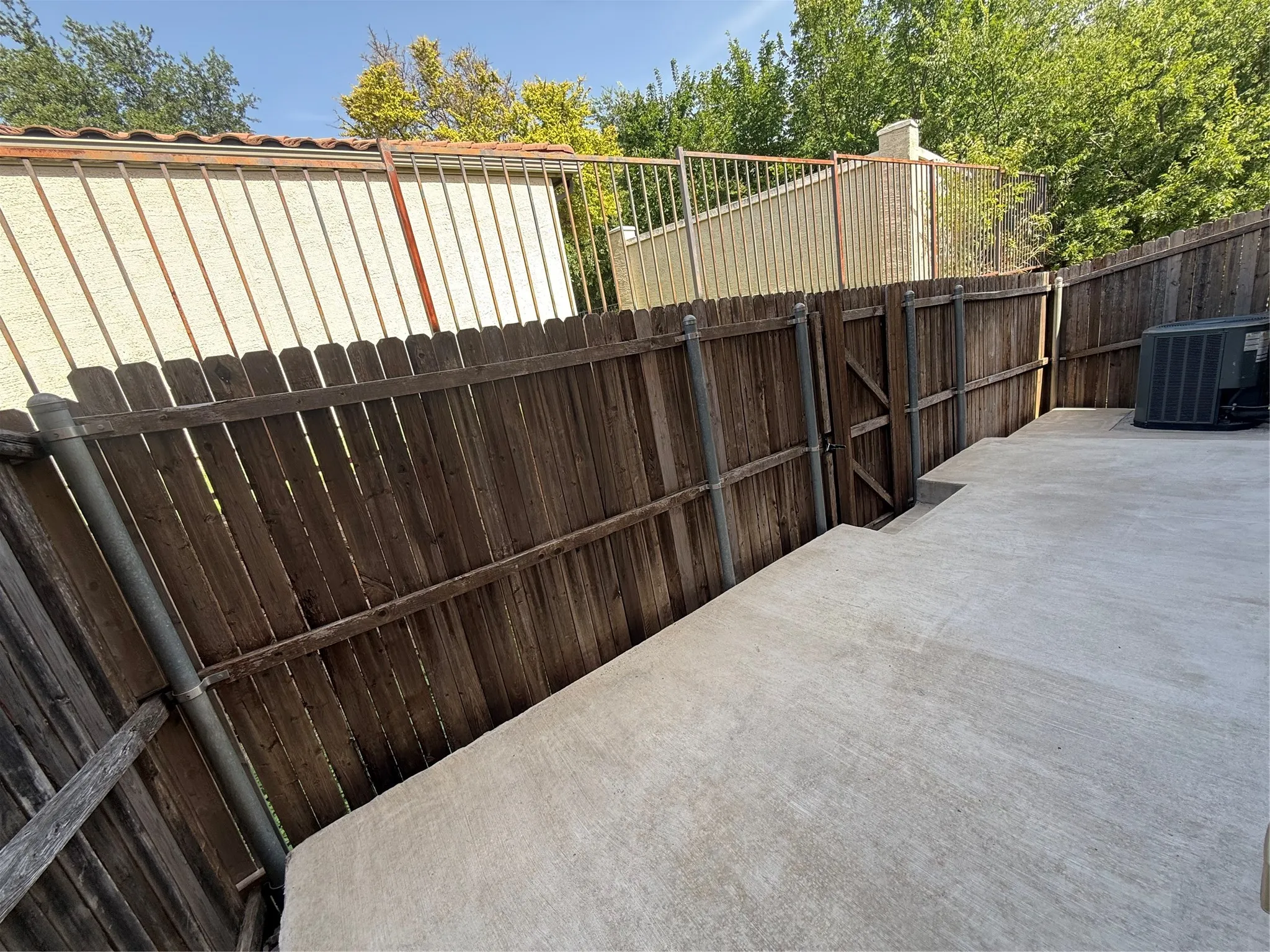 Concrete patio area featuring a wooden privacy fence, a functional gate, and a visible HVAC unit