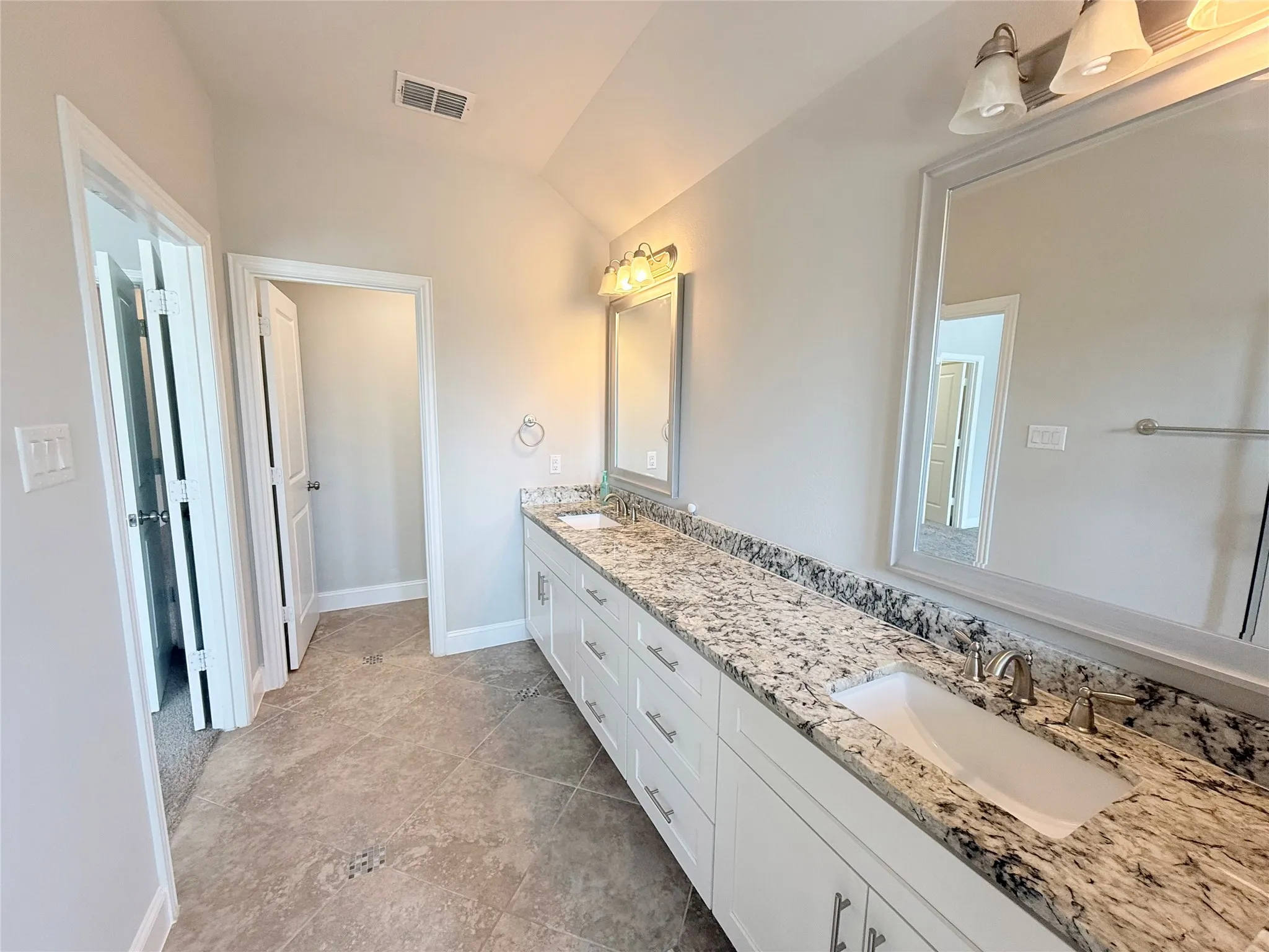 Expansive double vanity with a stone countertop, dual undermount sinks, white cabinetry, and brushed nickel hardware