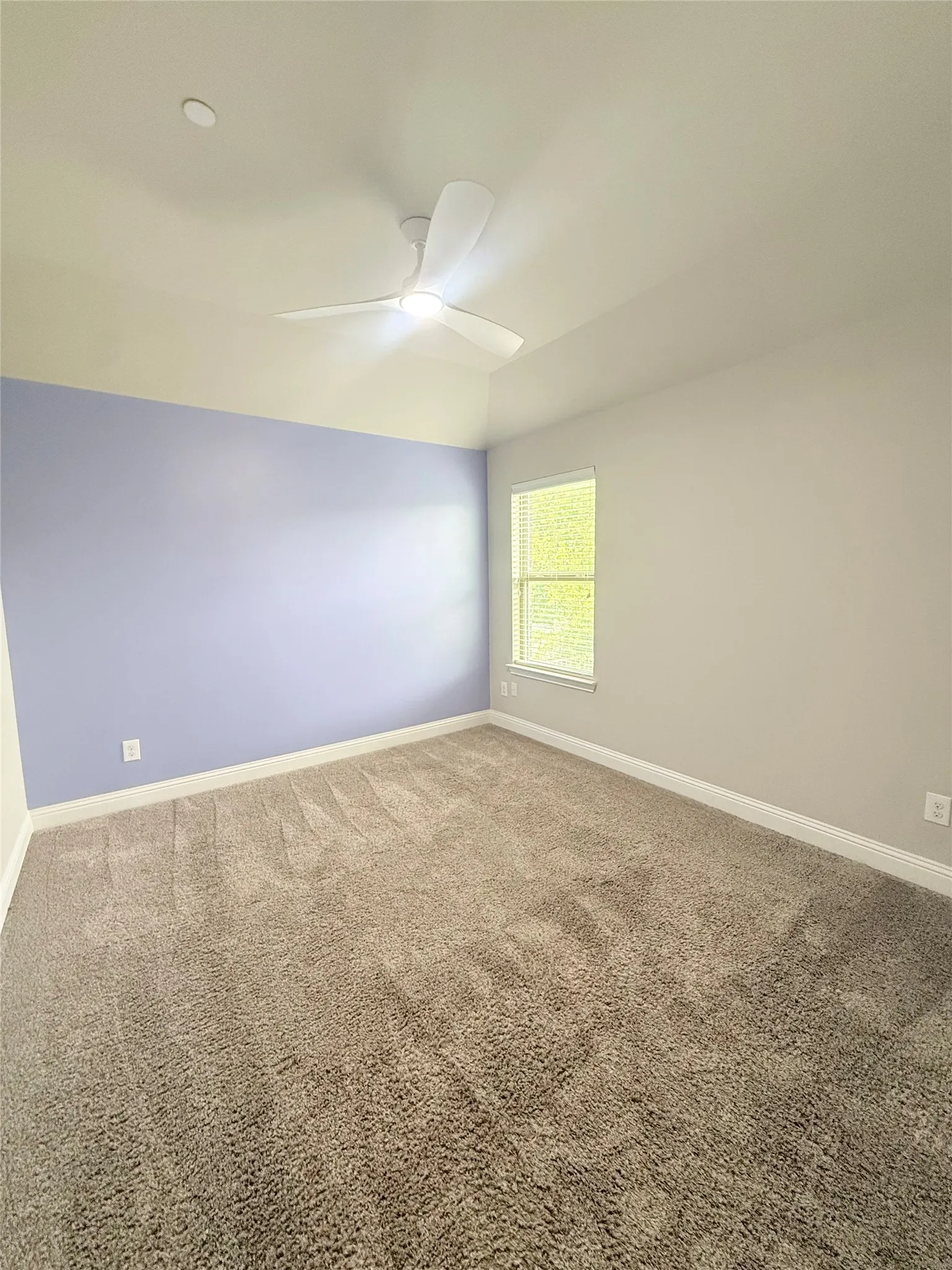 Spacious room featuring vaulted ceilings, a contemporary ceiling fan, plush carpeting, and a window with blinds