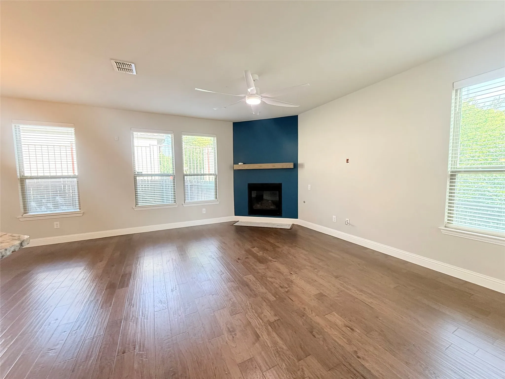 Spacious room featuring wood-finish flooring, a contemporary ceiling fan, and multiple windows with blinds