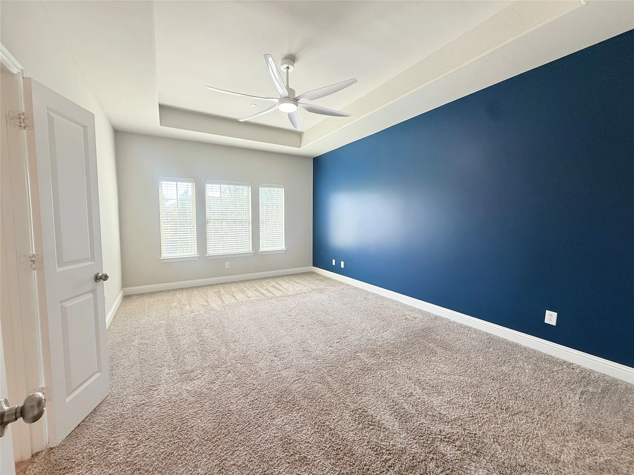 Spacious room featuring a tray ceiling, ceiling fan with integrated lighting, and carpet flooring