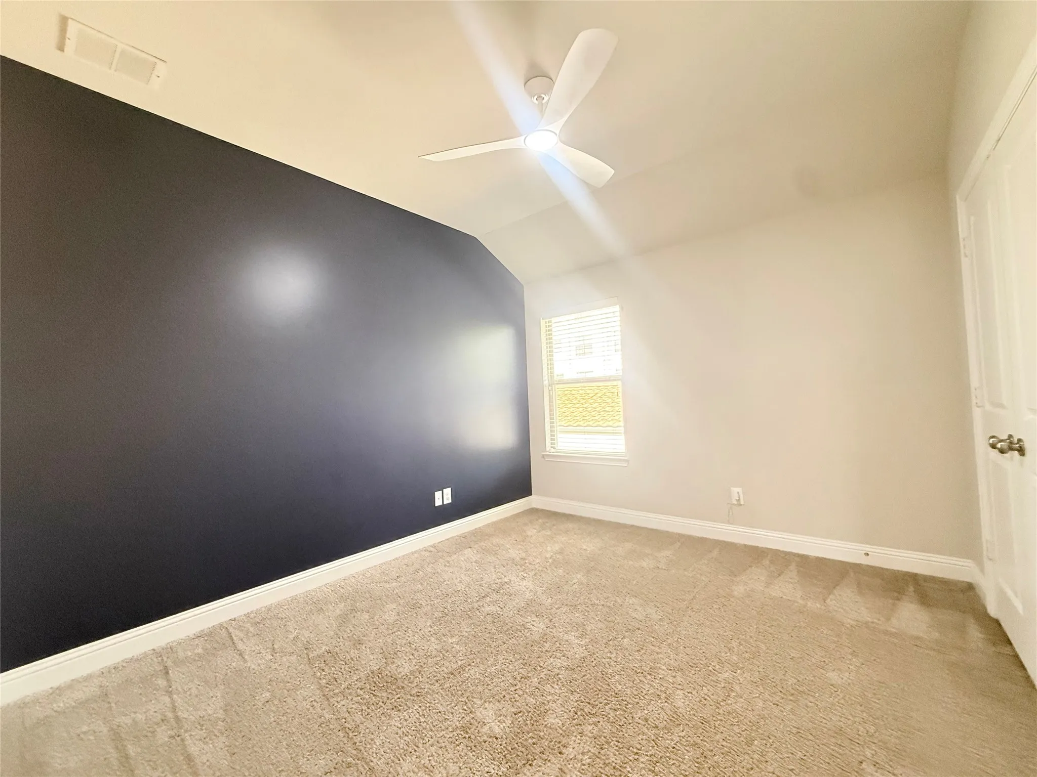 Room featuring a vaulted ceiling with a modern ceiling fan, dark accent wall, light-colored carpeting, a window with blinds, and white trim throughout