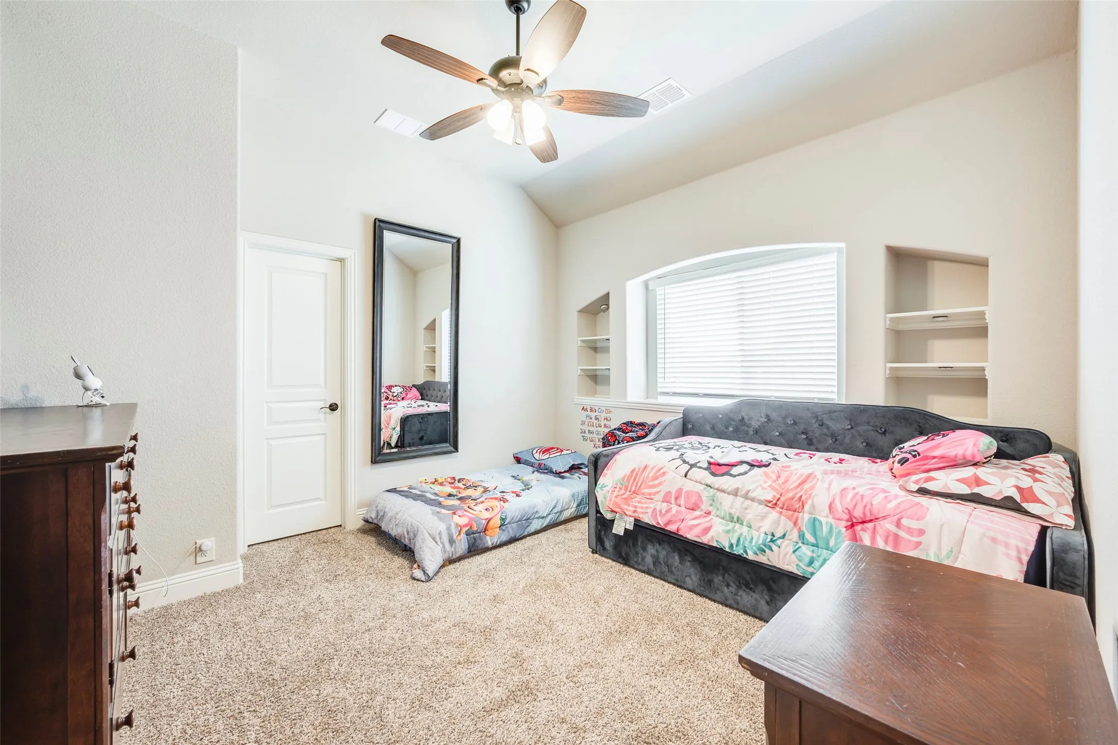 Vaulted ceiling with a ceiling fan, arched window with blinds, carpeted flooring, and built-in shelving