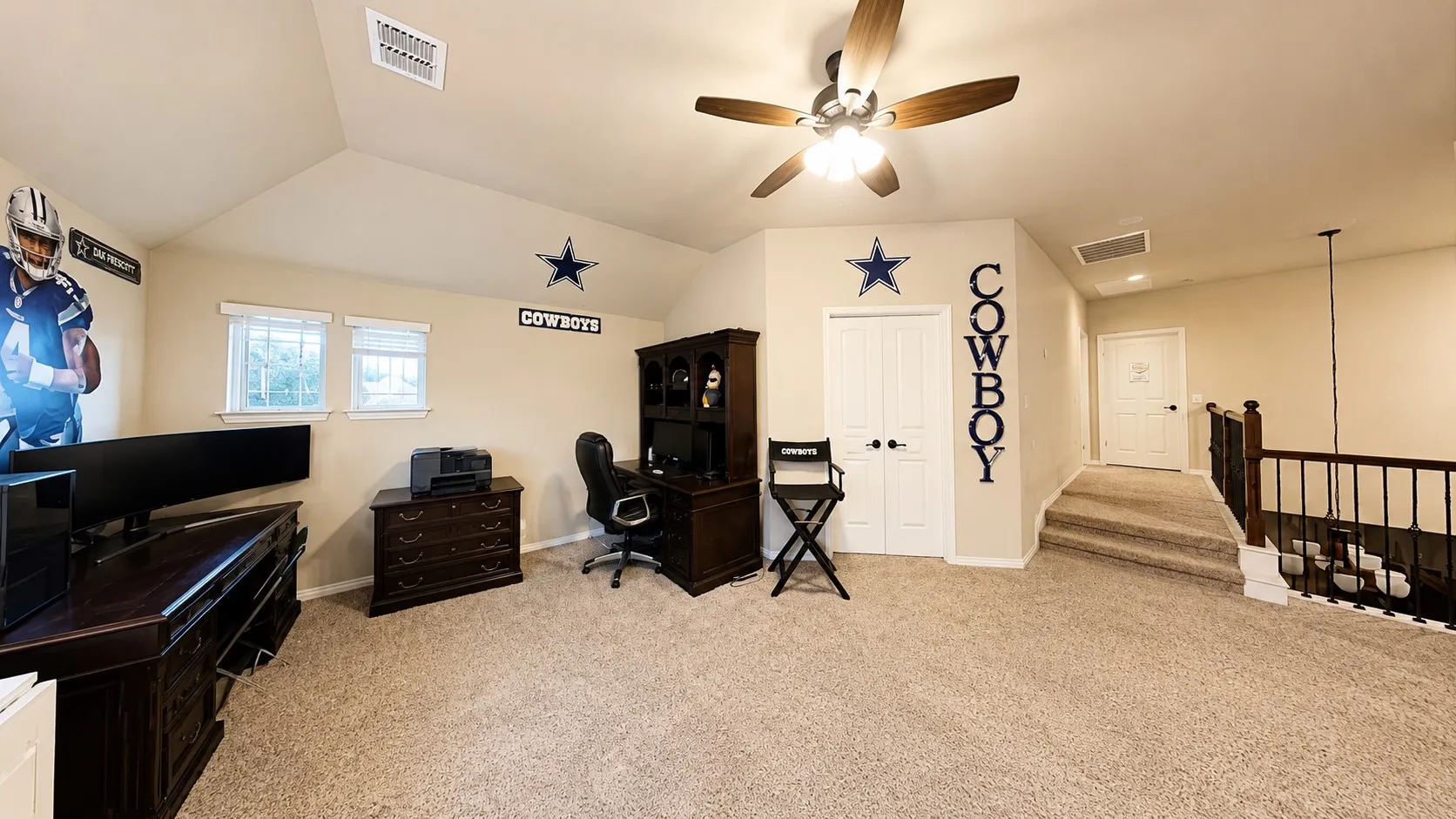 Carpeted room featuring a ceiling fan with integrated lighting, multiple windows, and a built-in staircase