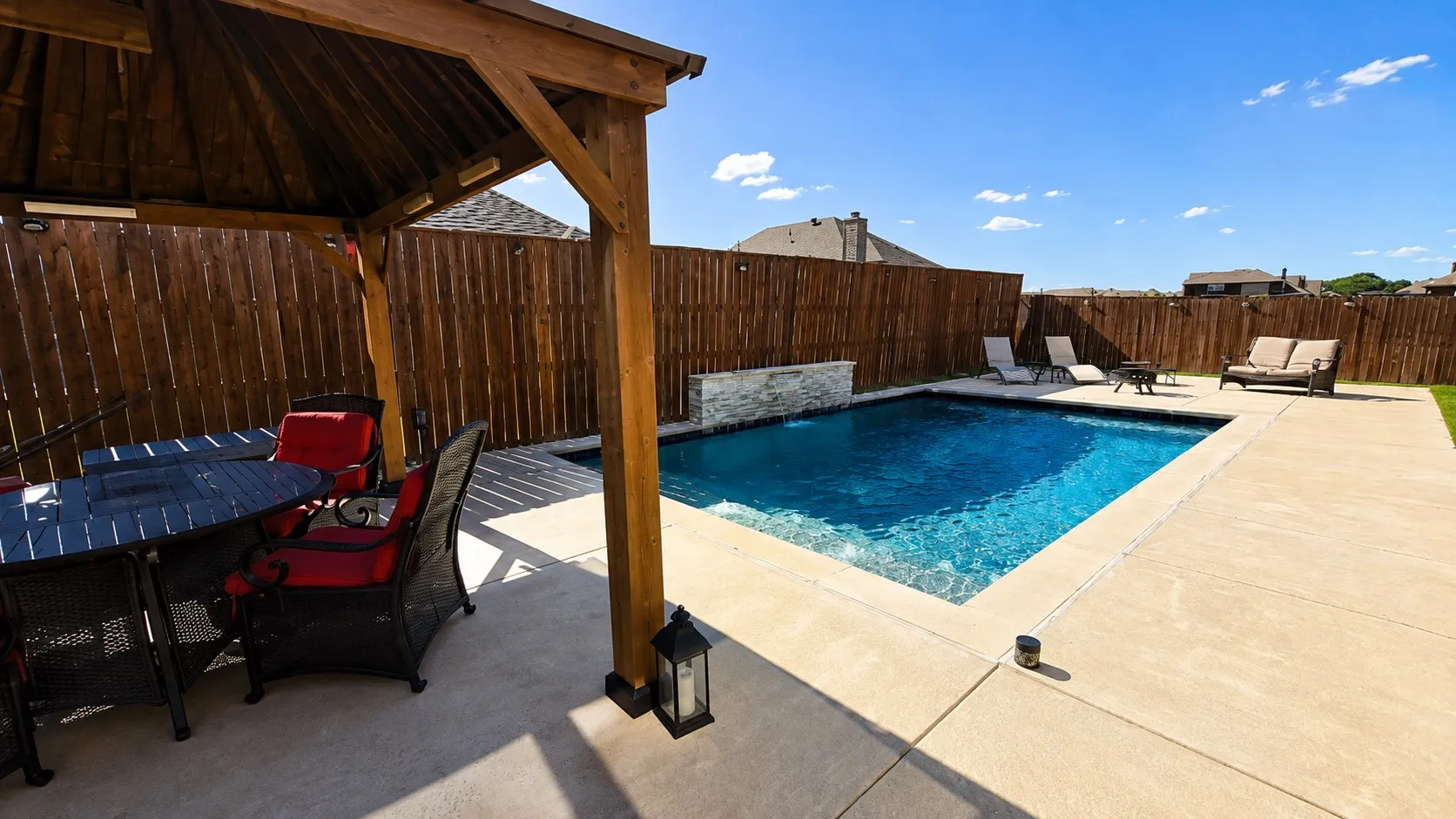 In-ground swimming pool with a stone-finish water feature, expansive concrete patio, and a wood-framed gazebo